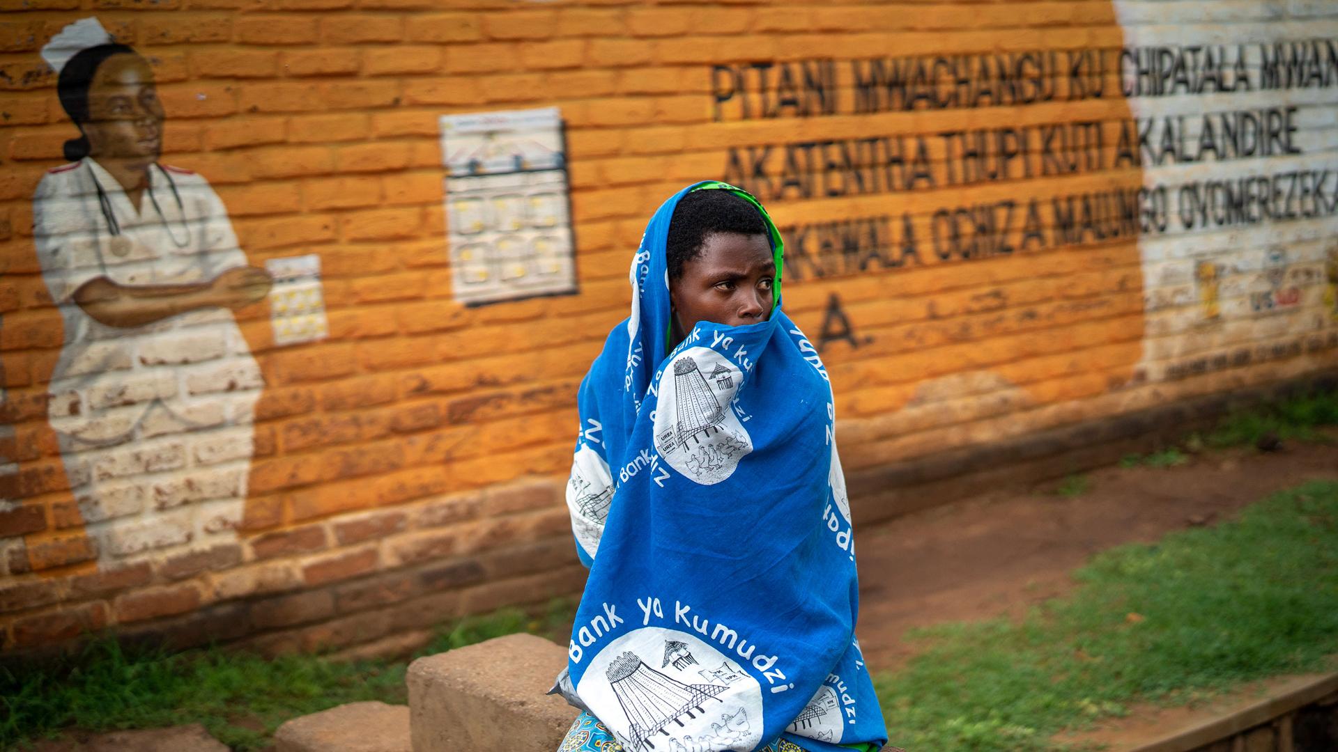 In this Tuesday, Dec. 10, 2019, file photo, a woman waits outside the Migowi Health Clinic to be injected with the world's first vaccine against malaria in a pilot program, in Migowi, Malawi. 