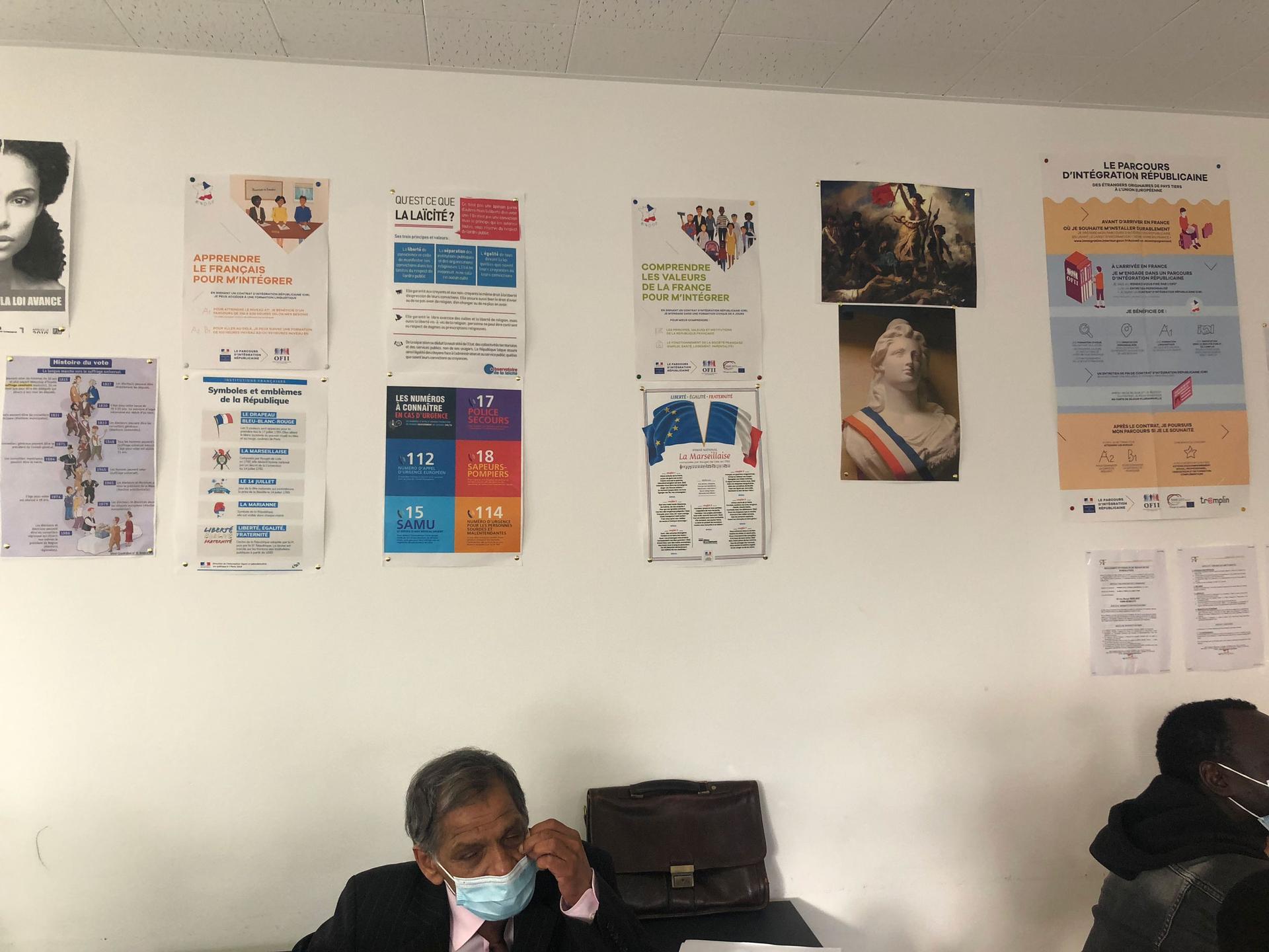 A man sits under posters of French images on a classroom wall inside a training session on French values.