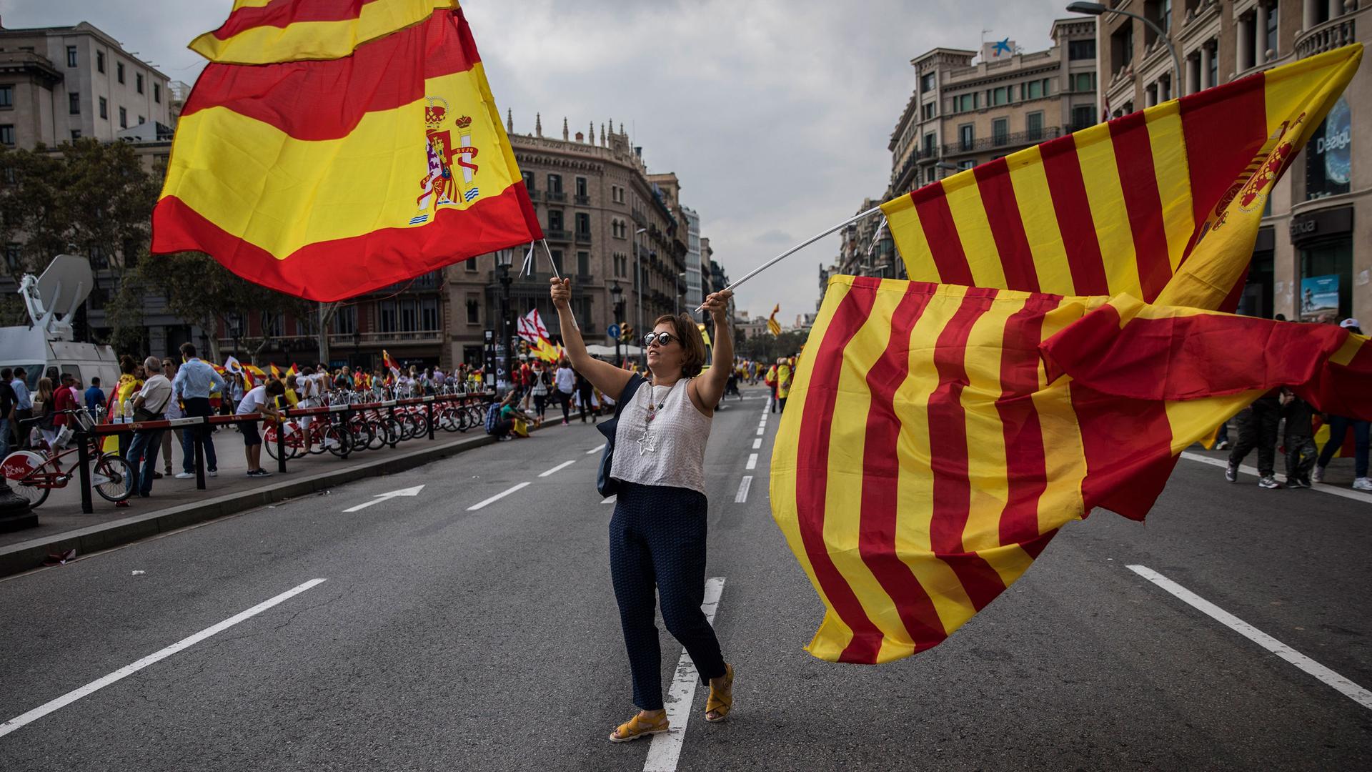 A woman waves flags of Catalonia and Spain as people celebrate a holiday known as "Dia de la Hispanidad" or Spain's National Day in Barcelona, Spain, Thursday, Oct. 12, 2017. 