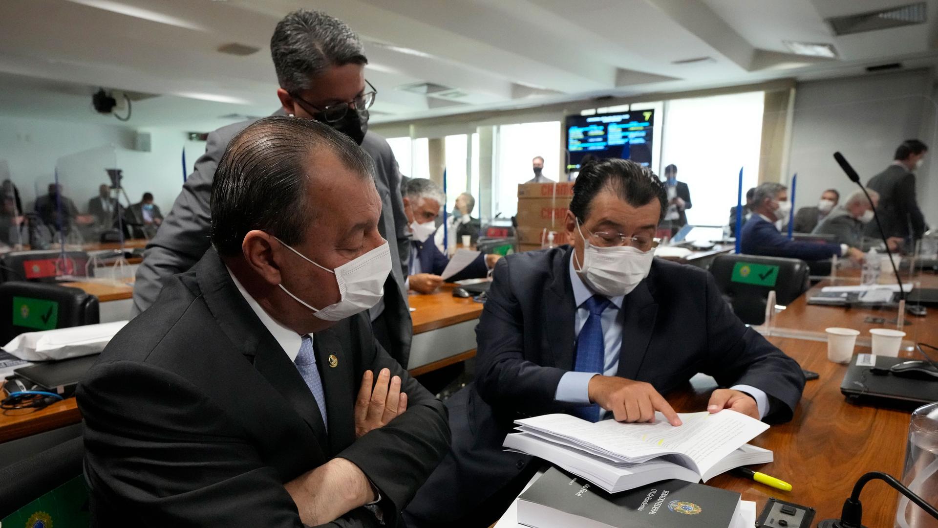 Senators Omar Aziz, sitting left, and Eduardo Braga, right, read a part of a report by a Senate commission that investigated the government's management of the COVID-19 pandemic at the Federal Senate in Brasilia, Brazil, Wednesday, Oct. 20, 2021.