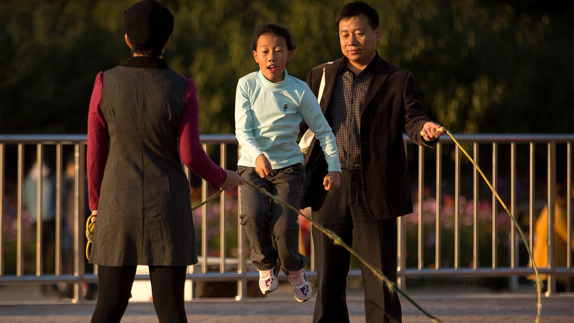 A man and woman twirl a jump rope for a girl at a park in Beijing