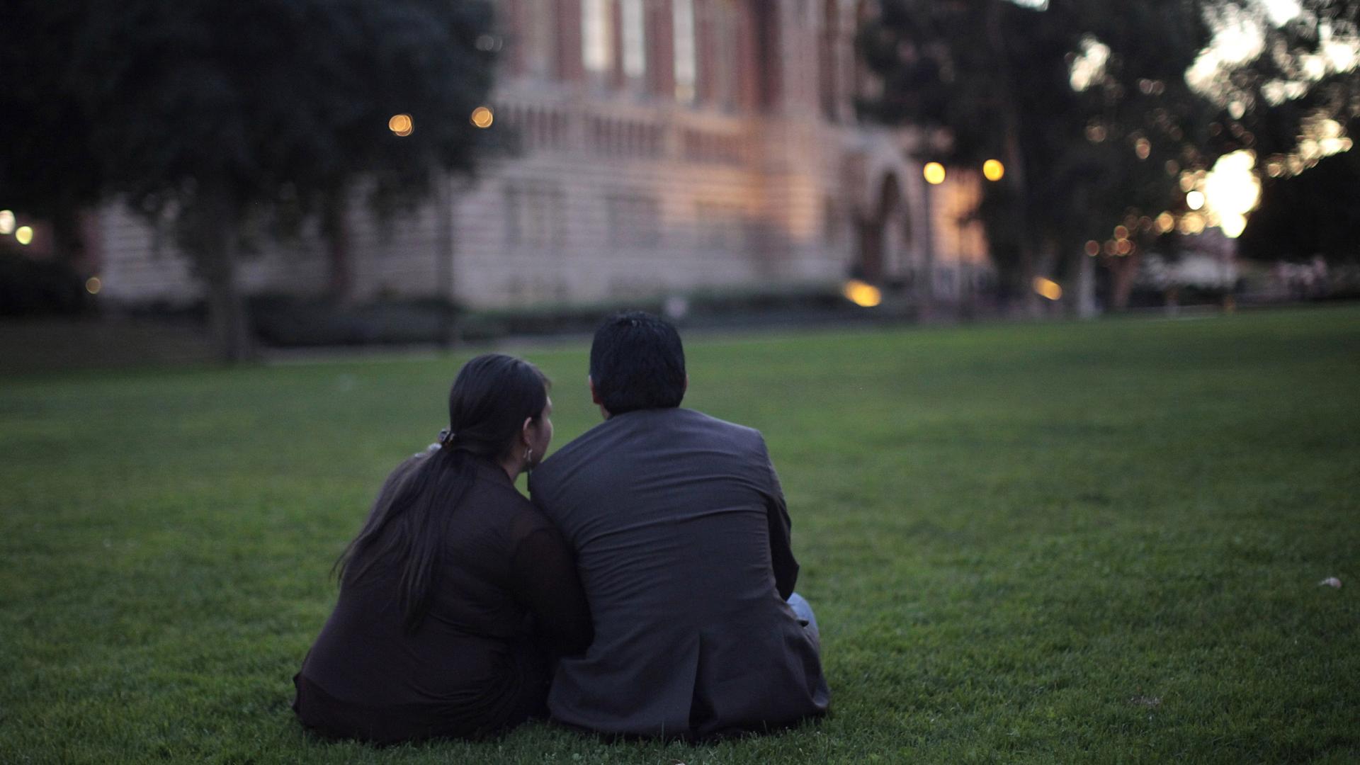 A man and a women sit on the grass together at twilight