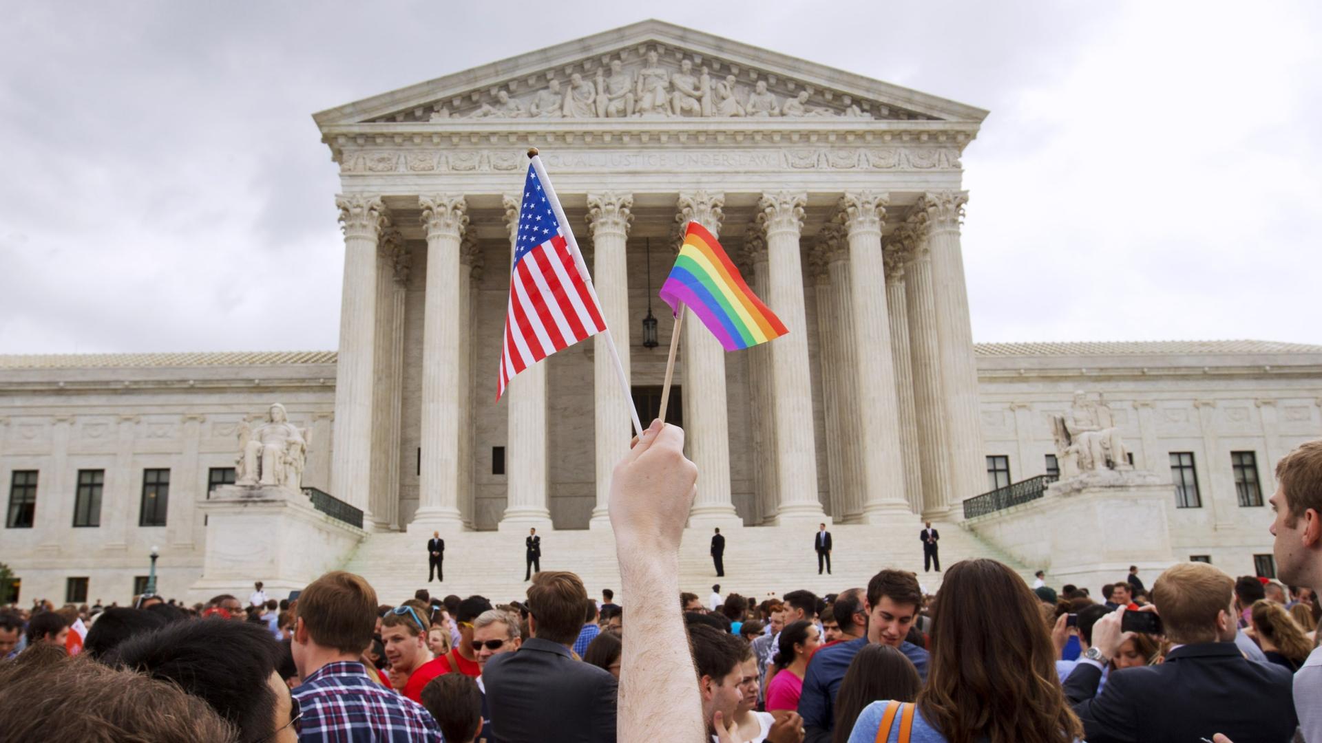 Arm holds up an American flag and a pride flag outside the US Supreme Court