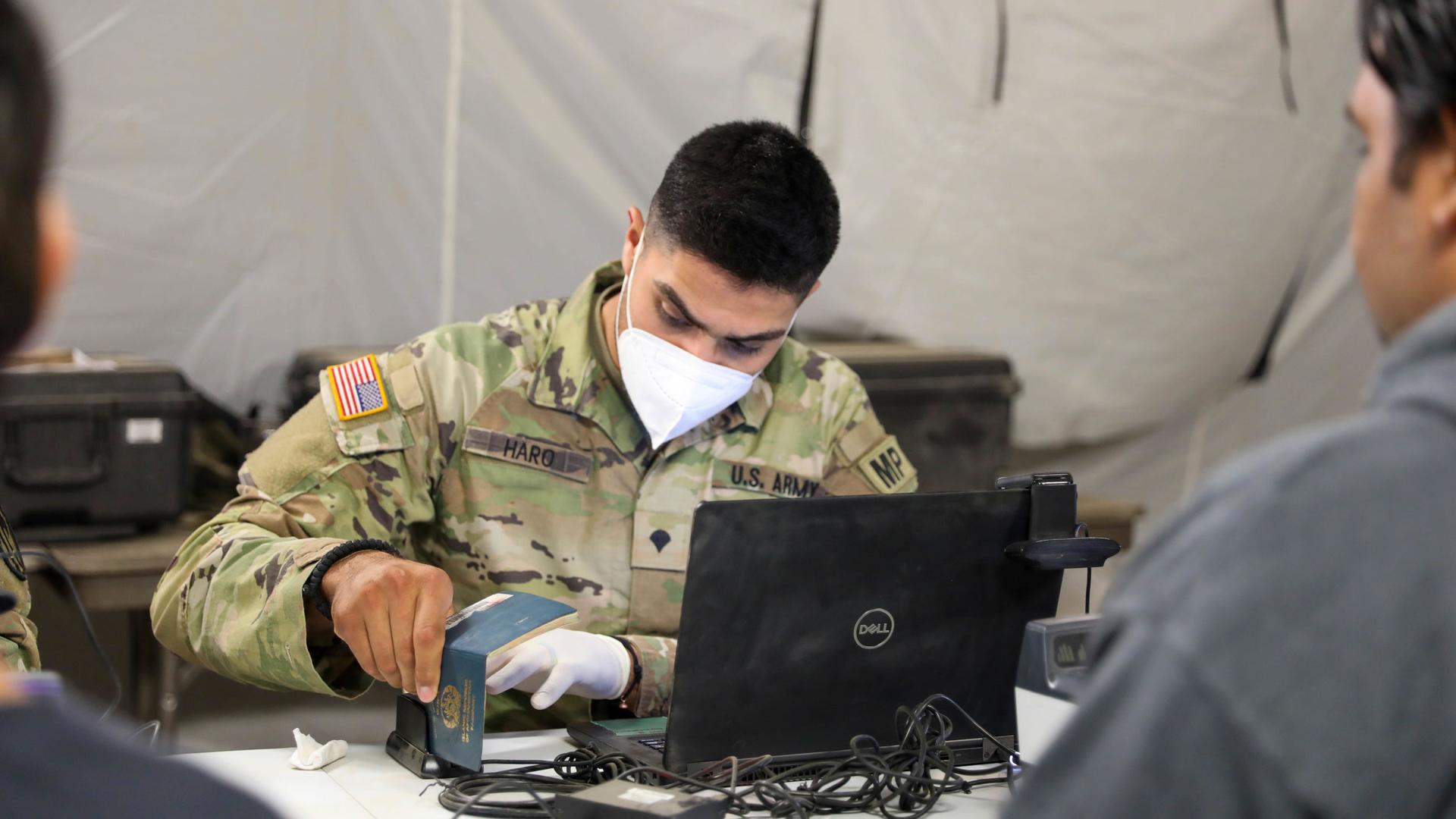In this image provided by the US Army, Spc. Alejandro Haro, military police, Task Force Ever Vigilant, scans documents as he checks-in Afghan evacuees at Camp Bondsteel, Kosovo, on Sept. 20, 2021. 