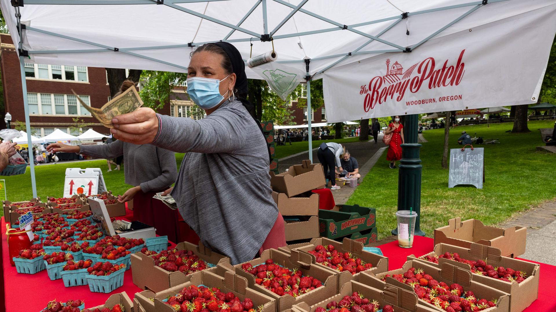 Nancy Sharabarin hands money to a customer buying strawberries at the Saturday farmers market as business opens up with a successful vaccination campaign in Portland, Oregon, Saturday, June 5, 2021.