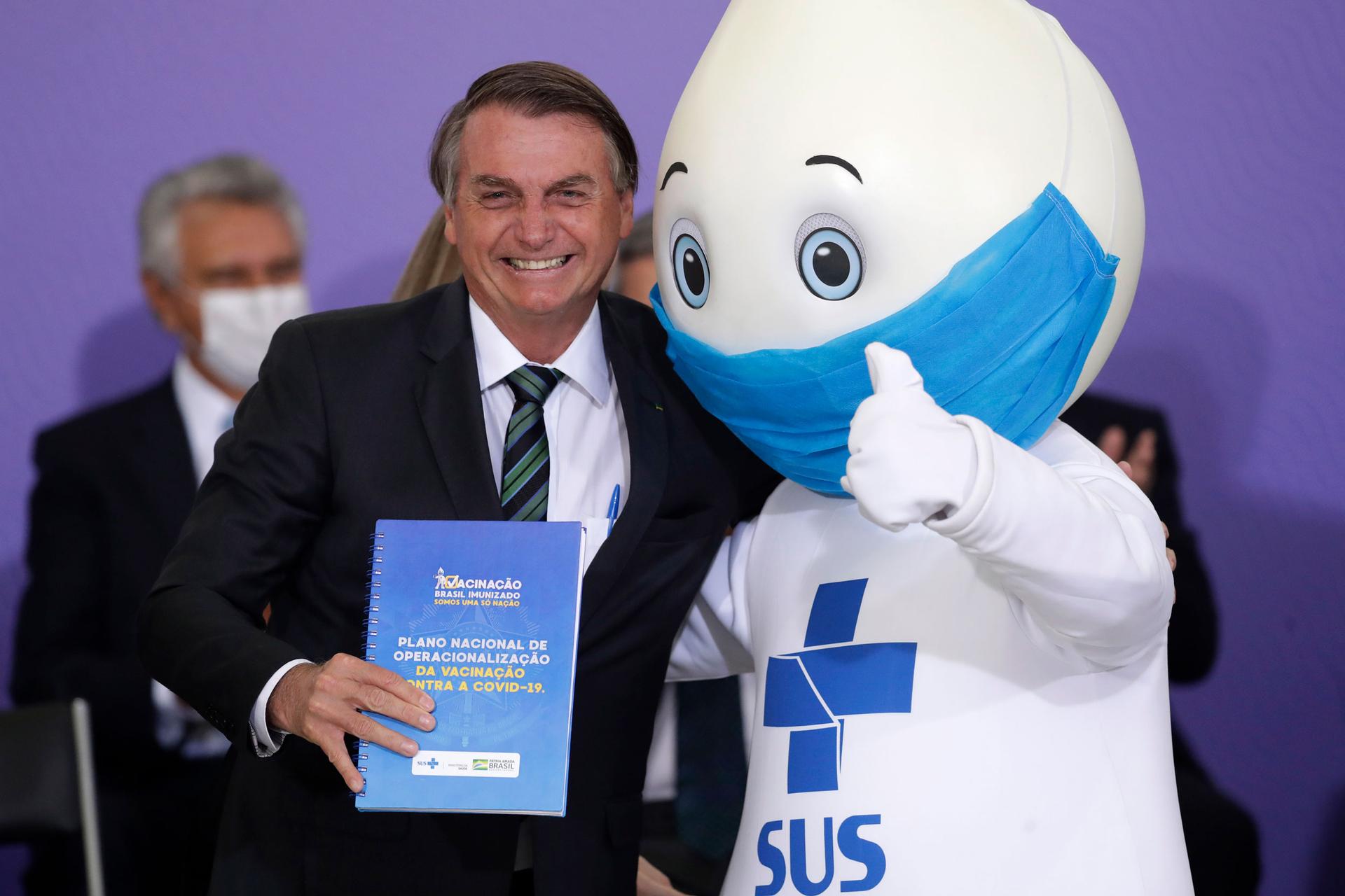 In this Dec. 16, 2020 file photo, Brazil's President Jair Bolsonaro poses for photos with the mascot of the nation's vaccination campaign, named 
