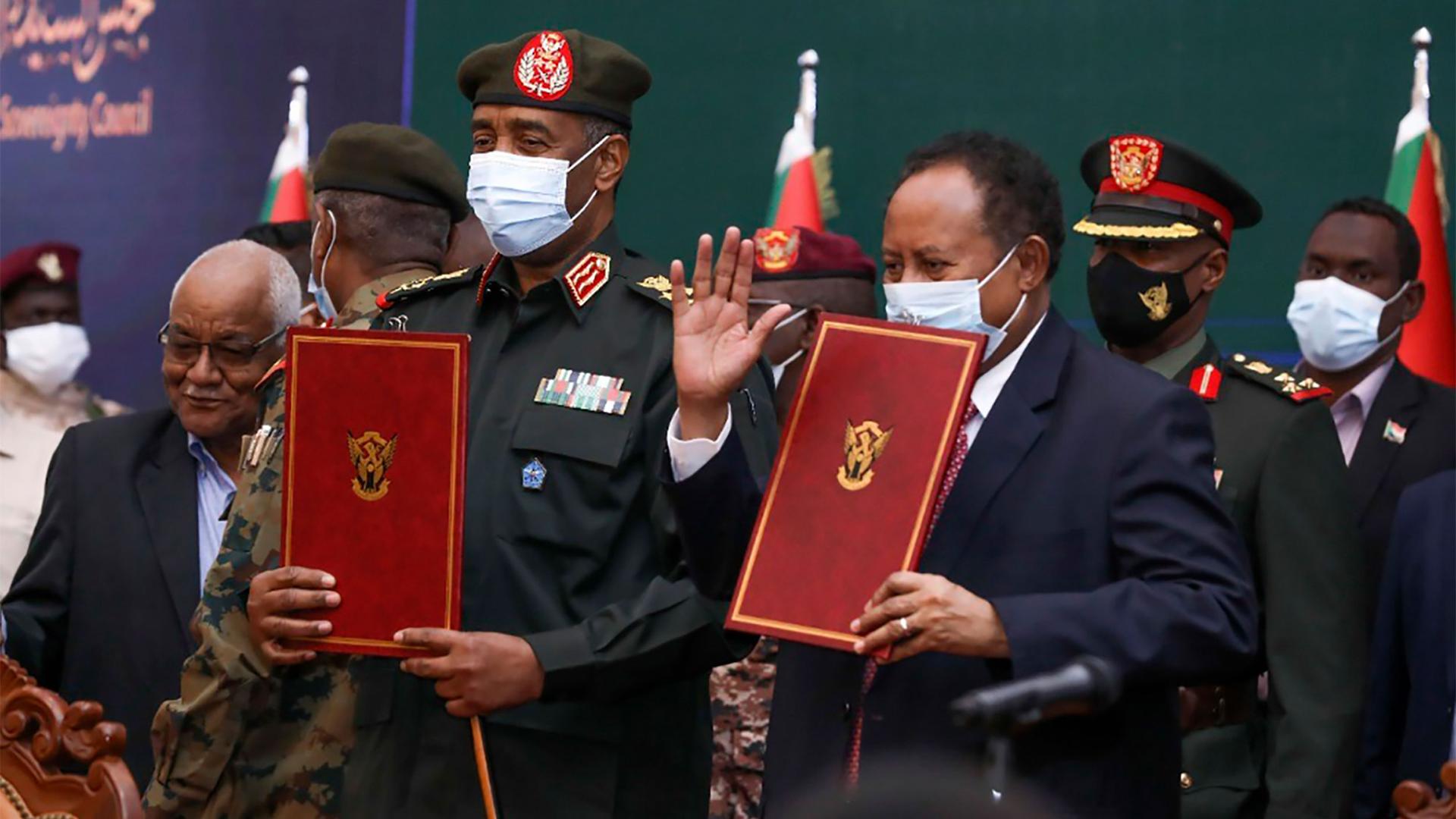 Sudan's top general Abdel Fattah al-Burhan and Prime Minister Abdalla Hamdok hold documents during a ceremony to reinstate Hamdok, who was deposed in a coup last month, in Khartoum, Sudan