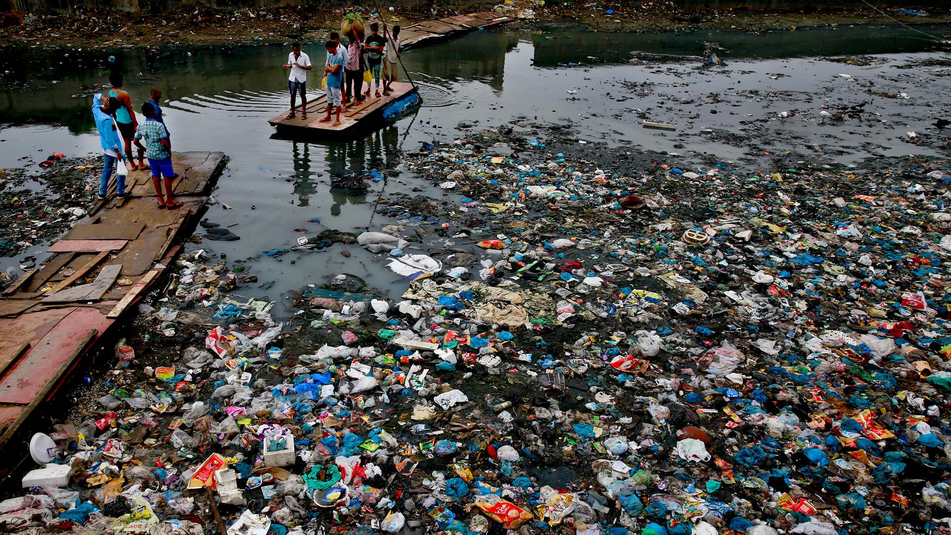 In this Sunday, Oct. 2, 2016 file photo, a man guides a raft through a polluted canal littered with plastic bags and other garbage in Mumbai, India.