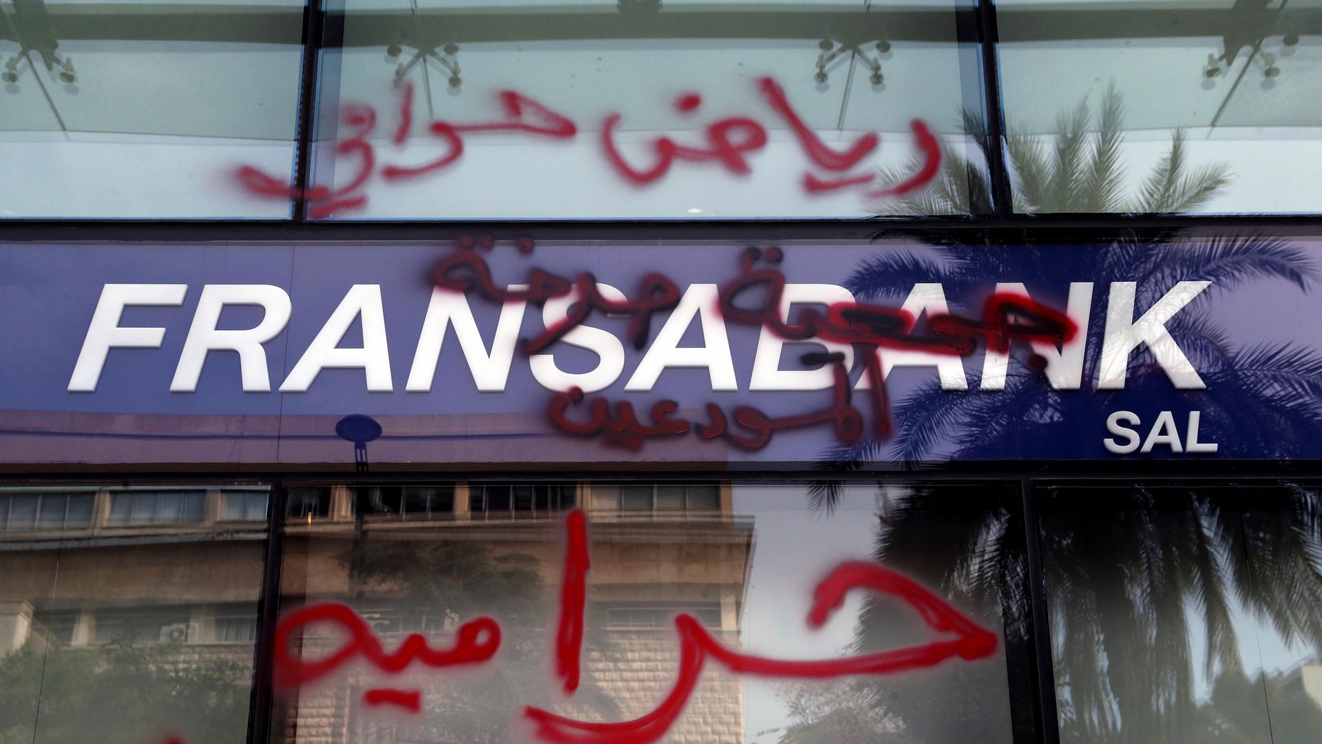 Bank customers write Arabic words thats read "Riad is a thief. Thieves" (Riad Salameh, the governor of Lebanon's Central Bank) on a facade of bank in Beirut, Lebanon, Friday, Nov. 19, 2021. 
