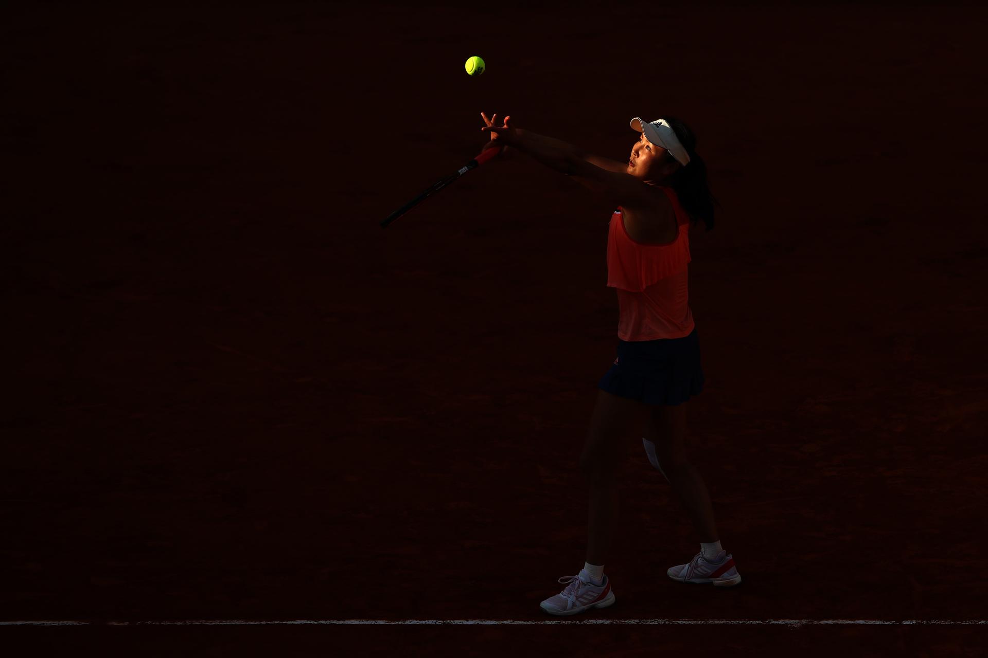 Tennis star Peng Shuai playing in the dark, with only her face and the ball brightly lit