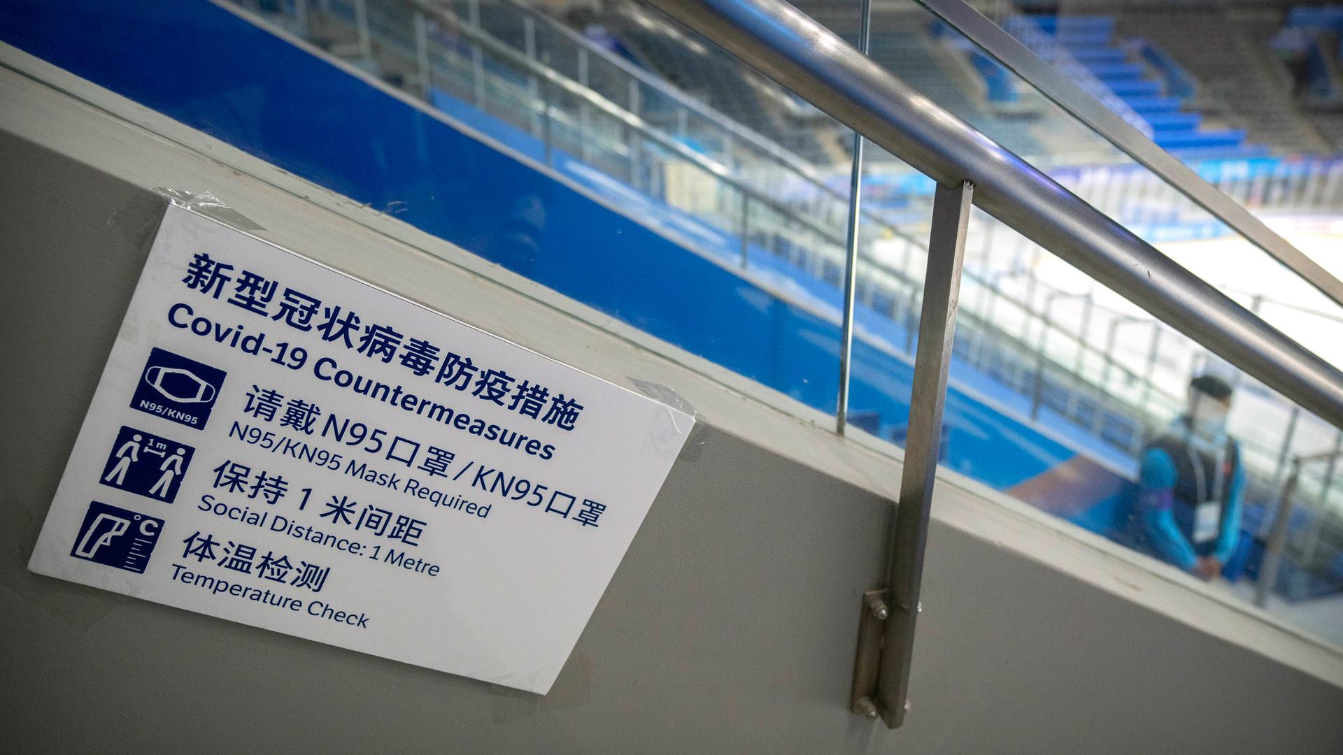 A staff member stands near a sign outlining COVID-19 protection measures during the Experience Beijing Ice Hockey Domestic Test Activity, a test event for the 2022 Beijing Winter Olympics, at the National Indoor Stadium in Beijing, on Nov. 10, 2021.