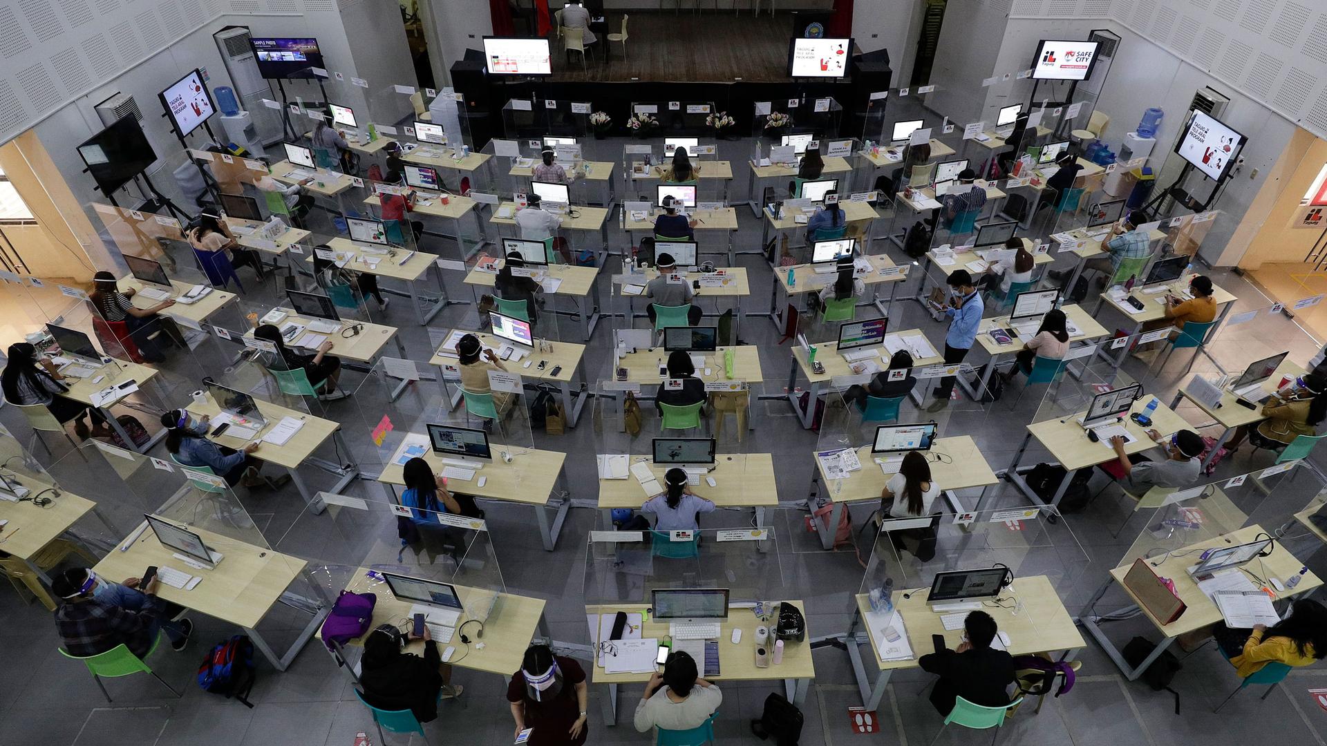 Teachers wearing face mask and face shield behind plastic barriers to prevent the spread of the coronavirus use computers during online classes at the Senator Renato "Companero" Cayetano (SRCC) Memorial Science and Technology High School in Taguig city, P