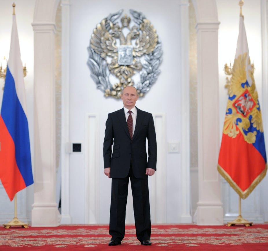 Russian President Vladimir Putin standing in front of country flags