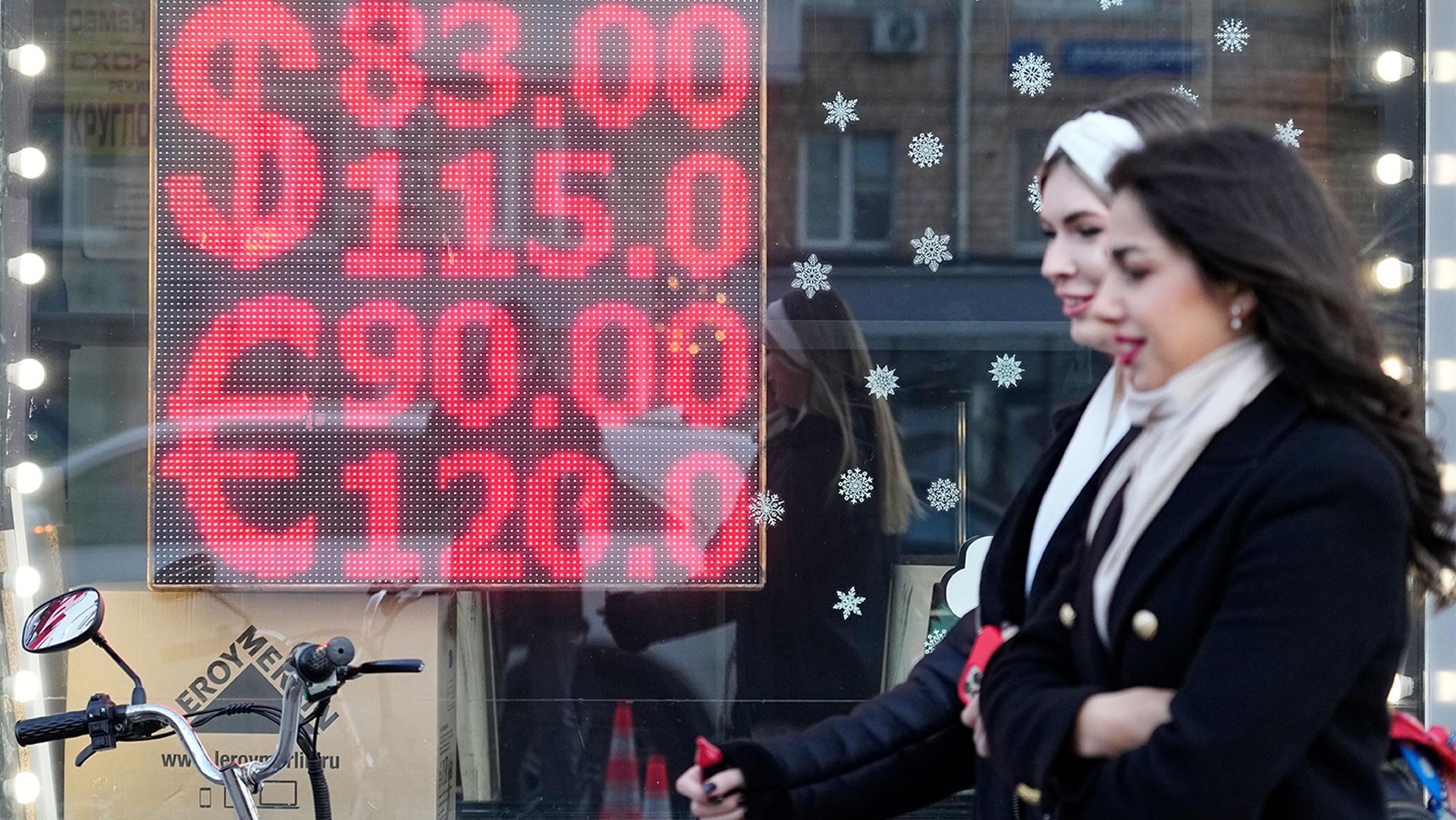 People walk past a currency exchange office screen displaying the exchange rates of U.S. Dollar and Euro to Russian Rubles in Moscow's downtown, Russia