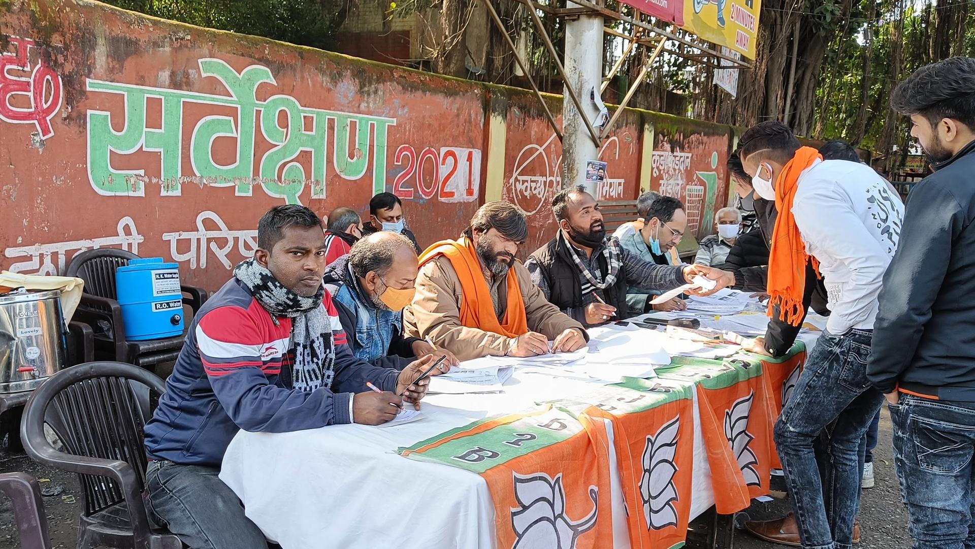 Several men supervise a voter registration table adorned with BJP flags during the election in Uttar Pradesh. 