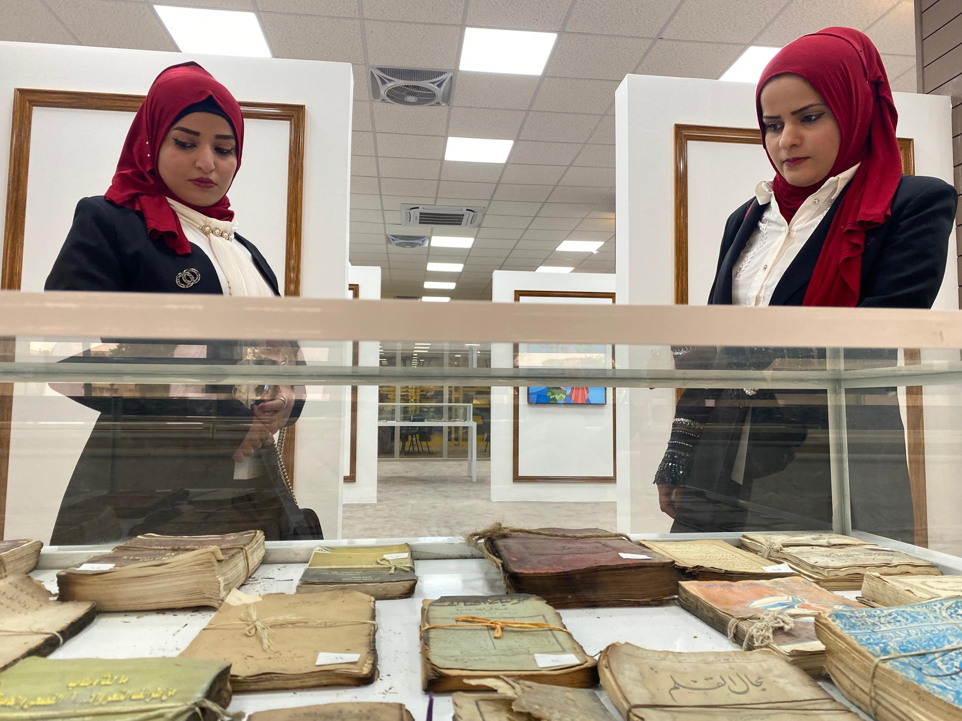 Ghufran Abdelmalek (right) and her sister Rahma Abdelmalek (left) peer at books salvaged from the ruins of the destroyed University of Mosul Central Library on Feb. 19, 2022. 