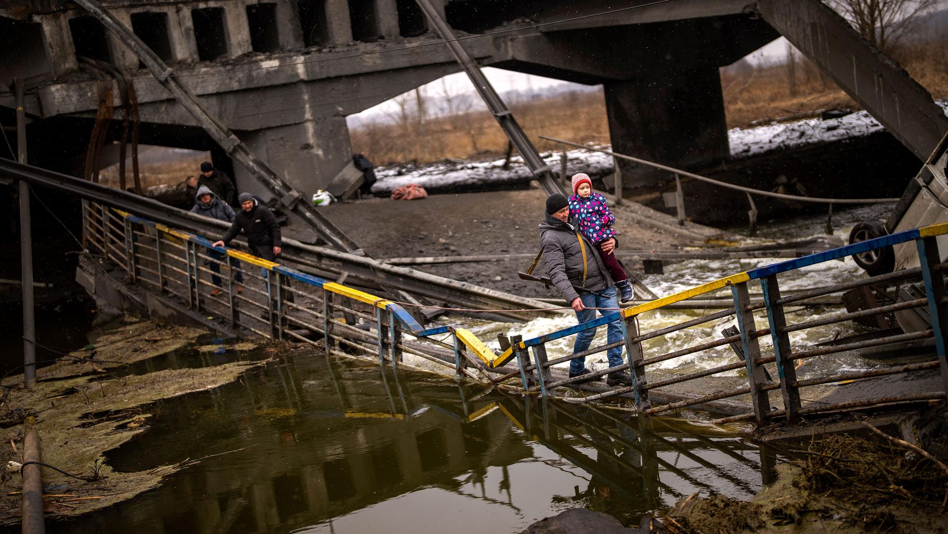 Local militiaman Valery, 37, carries a child as he helps a fleeing family across a bridge destroyed by artillery, on the outskirts of Kyiv, Ukraine, Wednesday, March 2. 2022. 