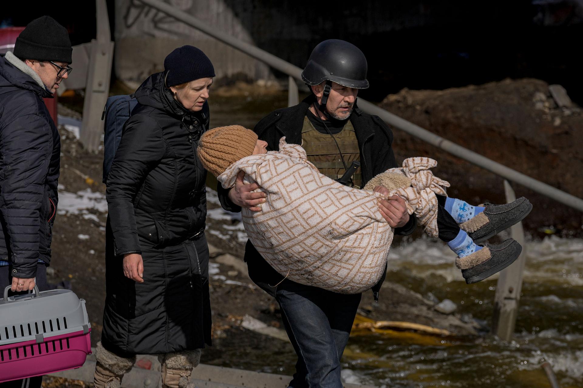 A man carries an elderly woman as people continue to leave Irpin, on the outskirts of Kyiv, Ukraine, Tuesday, March 8, 2022. 