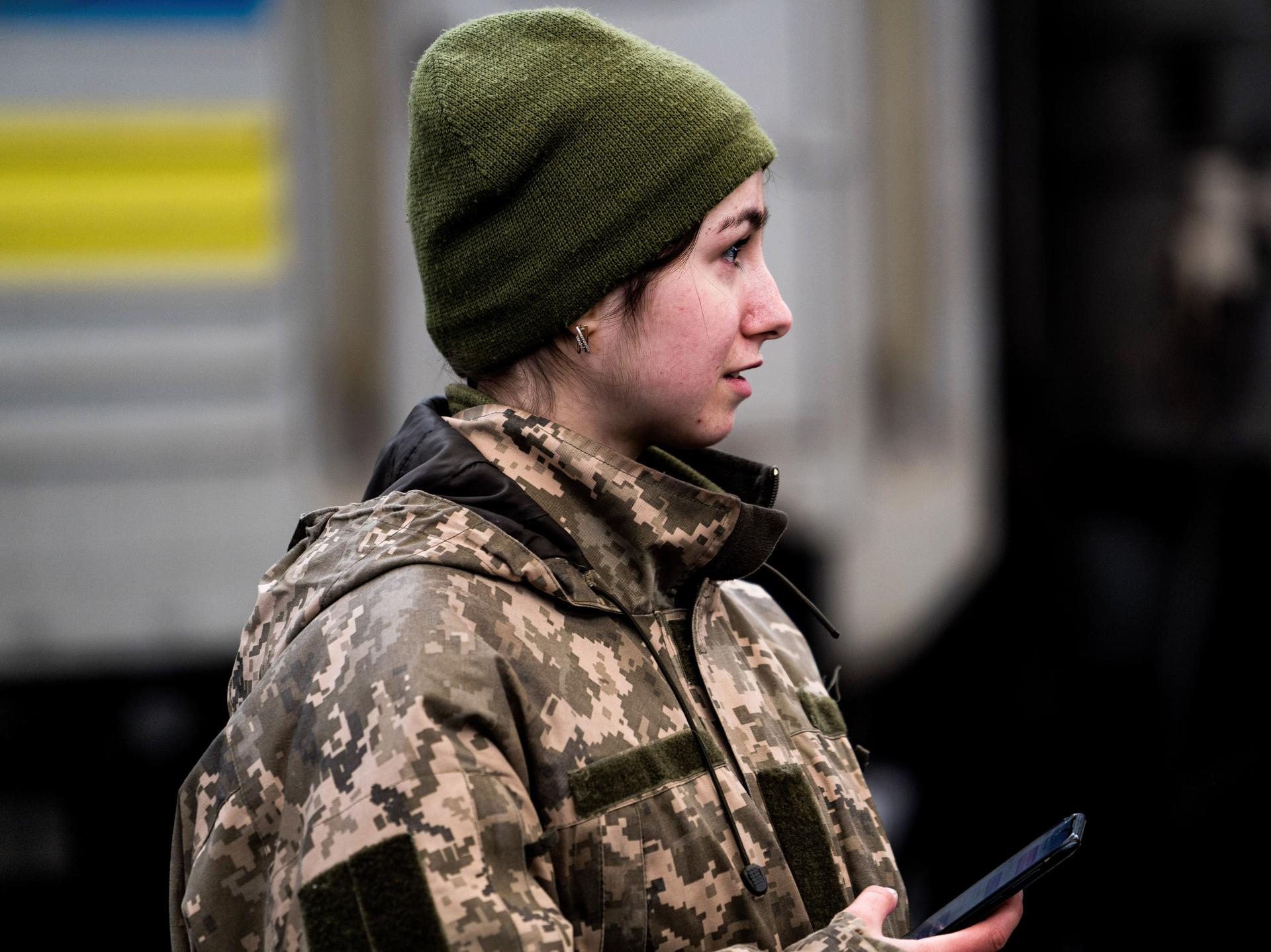 A woman Ukrainian soldier in combat fatigues at a train station