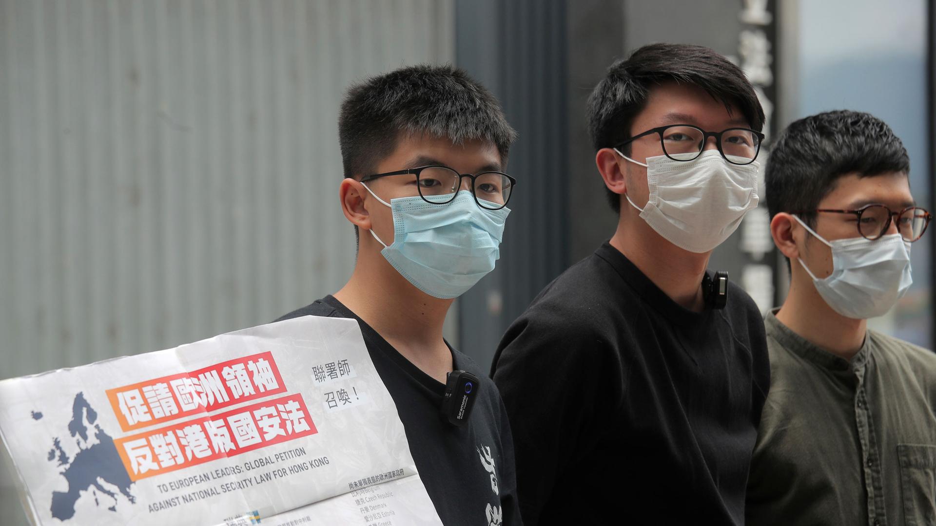 Pro-democracy activists, Joshua Wong, left, Sunny Cheung, center, and Nathan Law holding a placard, speak to media to urge the European leaders against national security law for Hong Kong outside the Legislative Council.