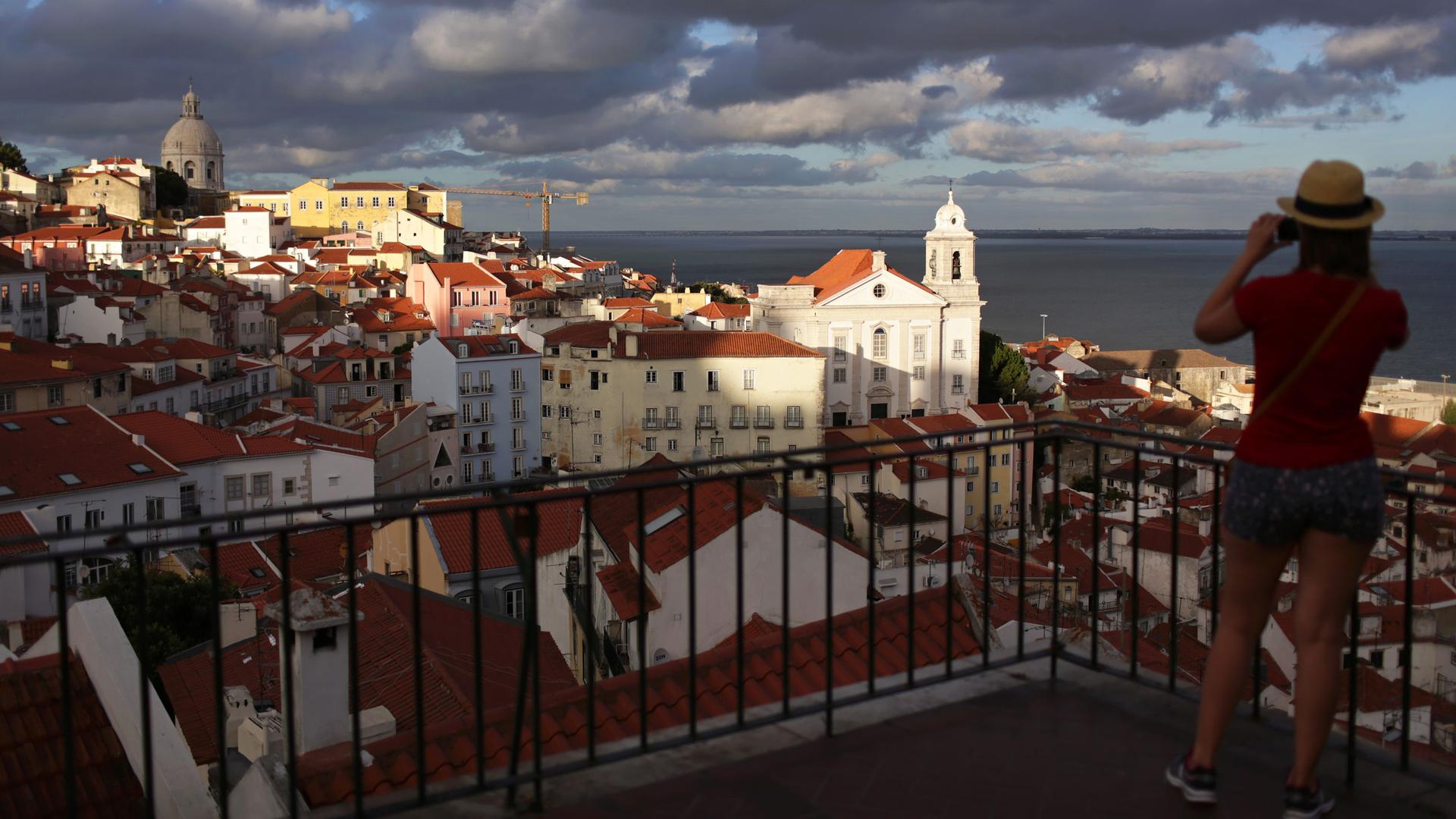 A young woman takes a picture of Lisbon's Alfama neighborhood from a viewpoint above it at sunset Saturday, Aug. 15, 2015.