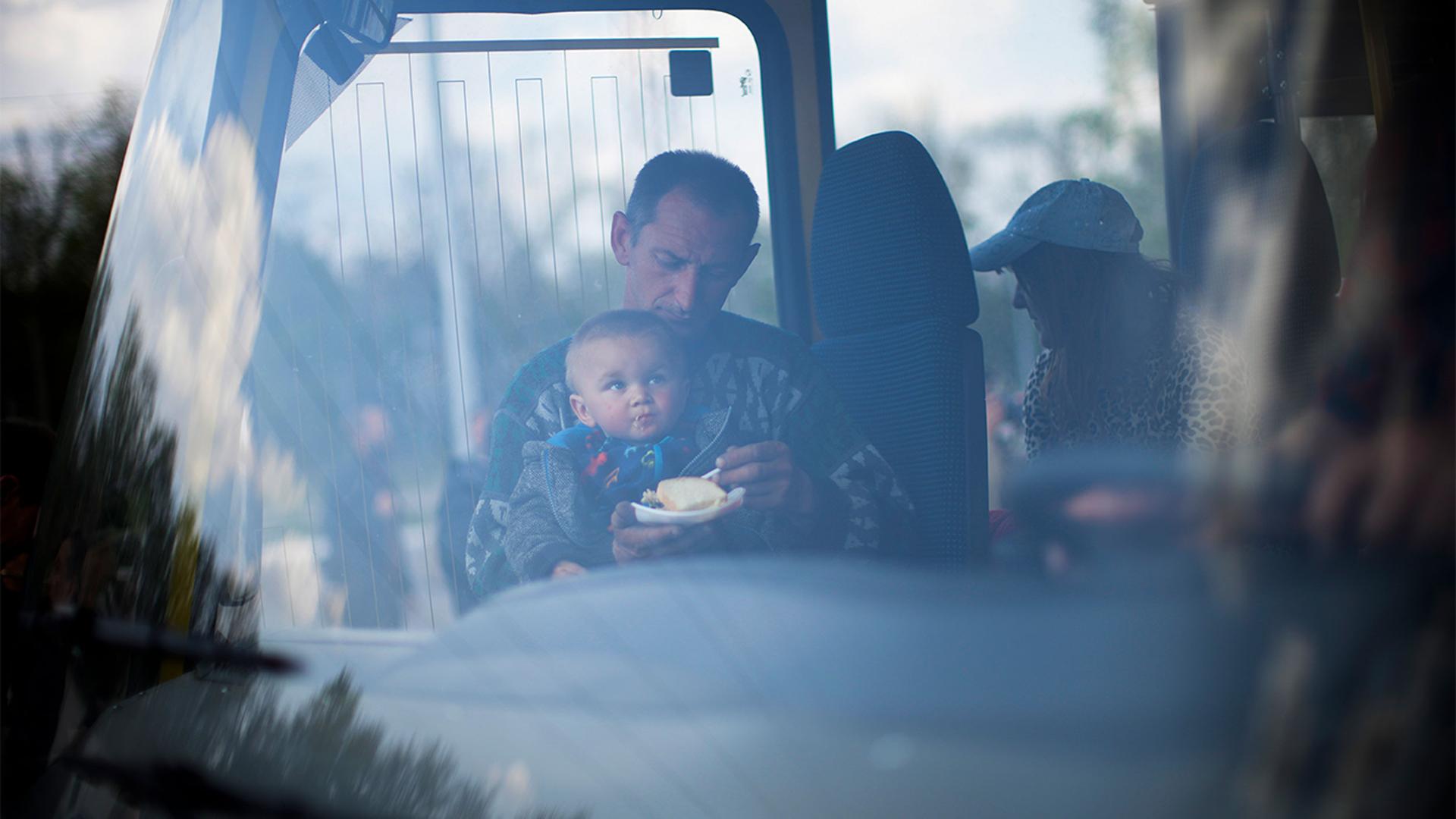 A man feeds a child as they arrive by bus at a reception center for displaced people in Zaporizhzhia, Ukraine