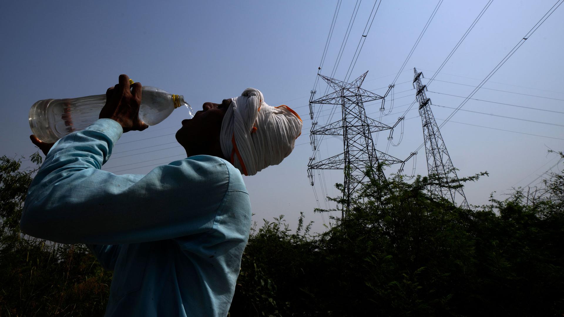 A worker quenches his thirst next to power lines as a heatwave continues to lashes the capital, in New Delhi, India, Monday, May 2, 2022. 