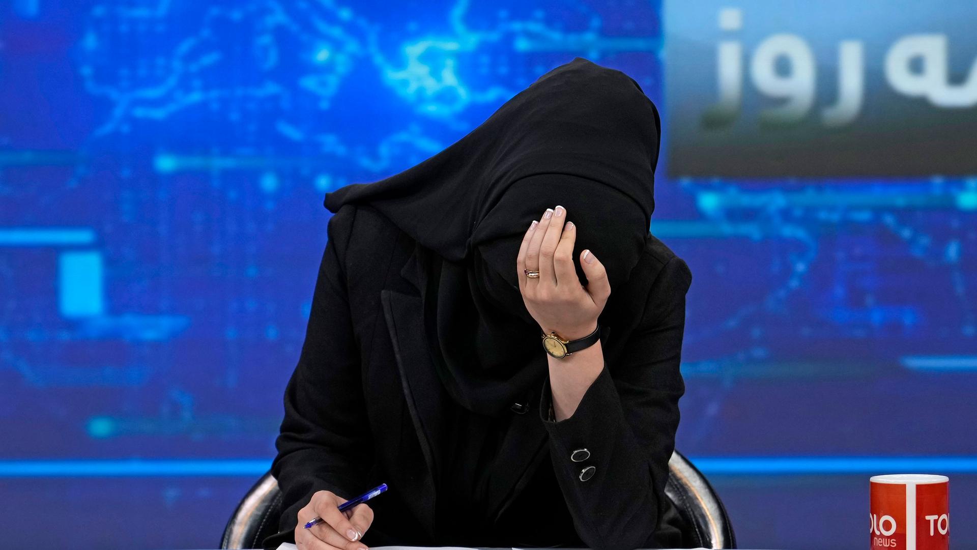 TV anchor Khatereh Ahmadi bows her head while wearing a face covering as she reads the news on TOLOnews, in Kabul, Afghanistan, Sunday, May 22, 2022. 