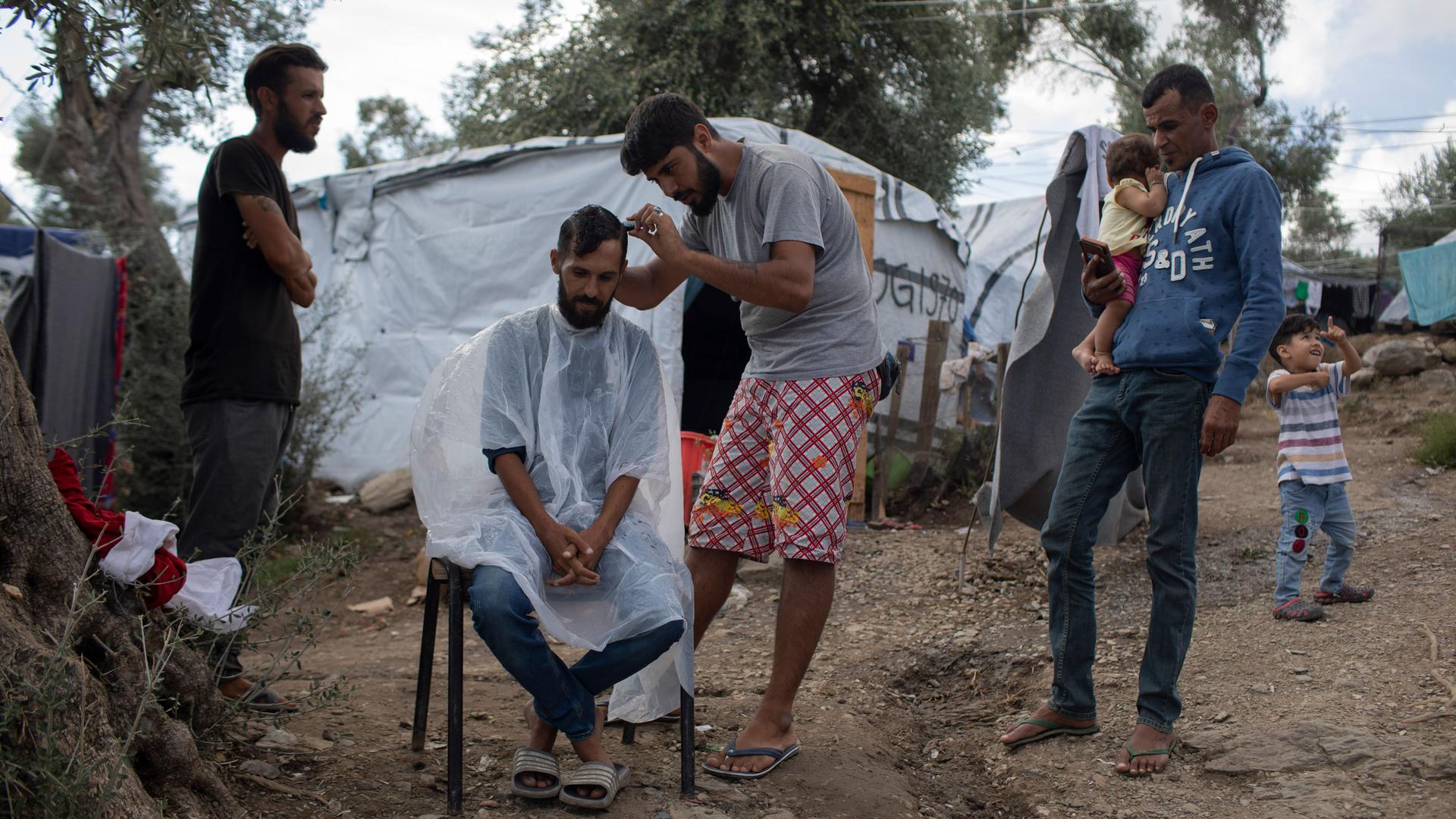 In this photo from 2019, Gasan, a 25-year-old Syrian, gives a hair cut to 31-year-old Ali from Baghdad, Iraq, in the overcrowded Moria refugee and migrant camp, Lesbos island, Greece.