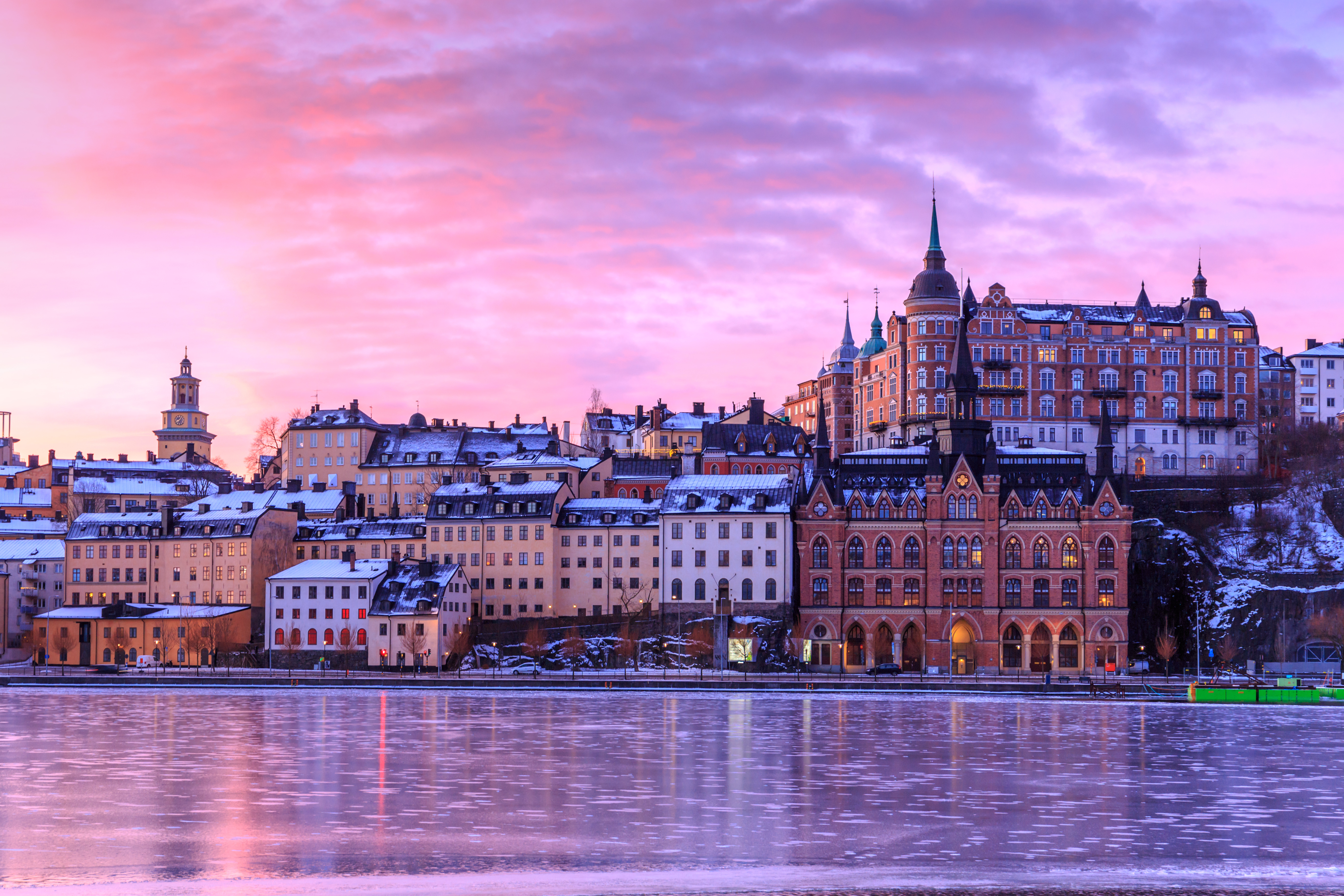 Photo of a Swedish city at sunset, with lights glowing in windows and reflecting into a fjord