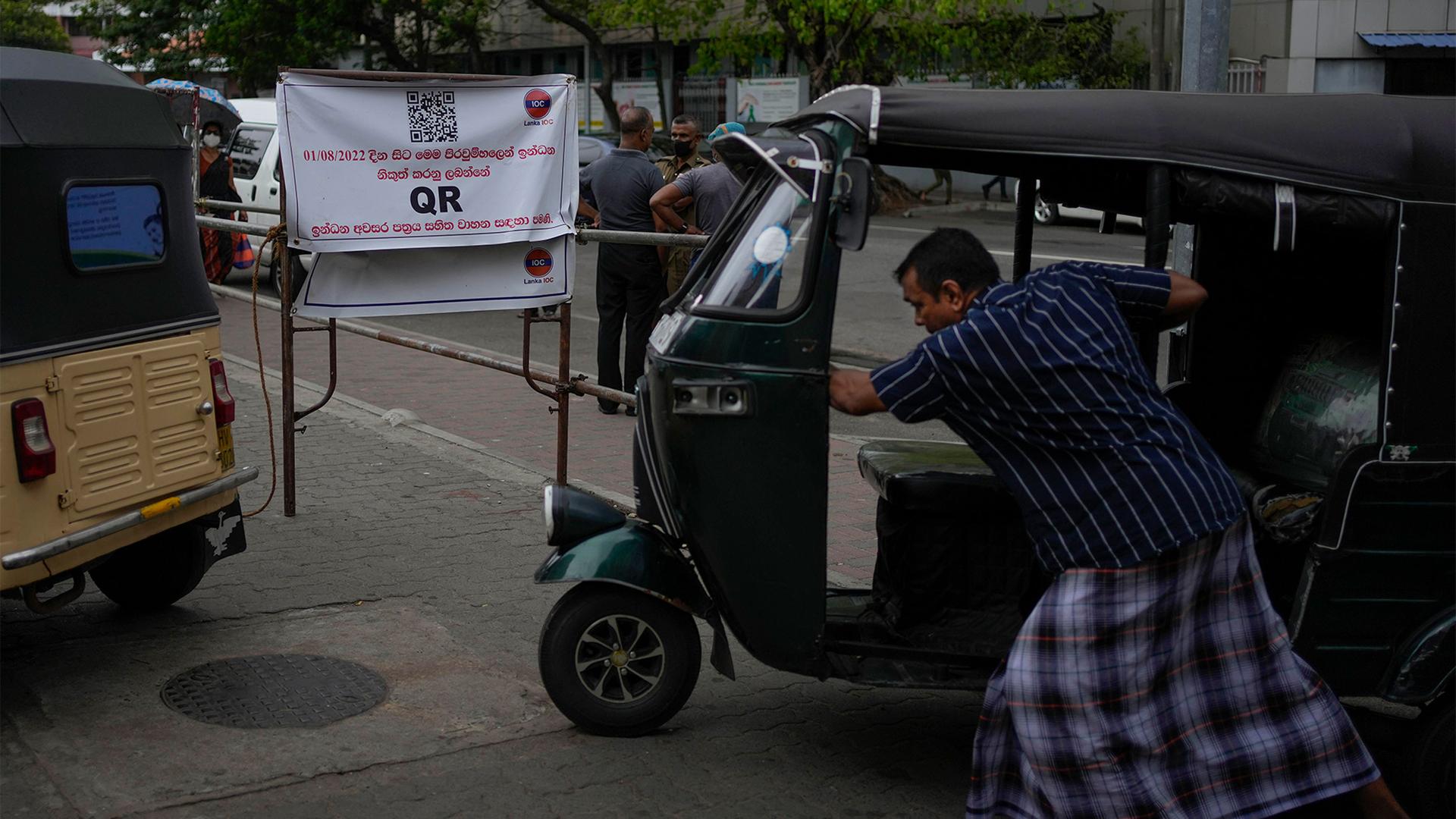 An auto rickshaw driver pushes his vehicle next to a banner that says only those vehicles with QR codes will be given fuel at a fuel station in Colombo, Sri Lanka