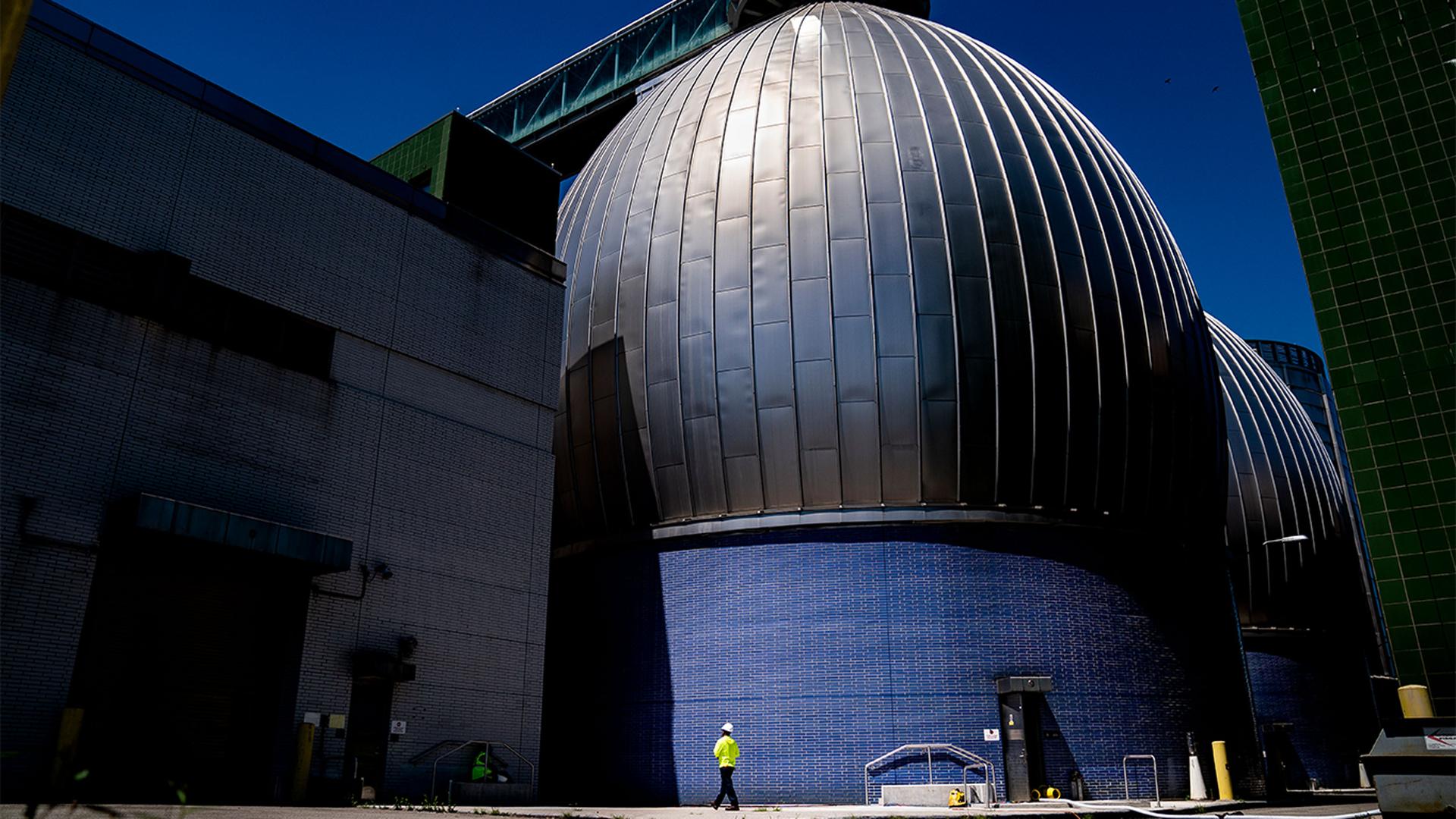 A worker walks alongside the Newtown Creek Wastewater Treatment Plant's array of digester eggs in the Greenpoint neighborhood of Brooklyn, New York