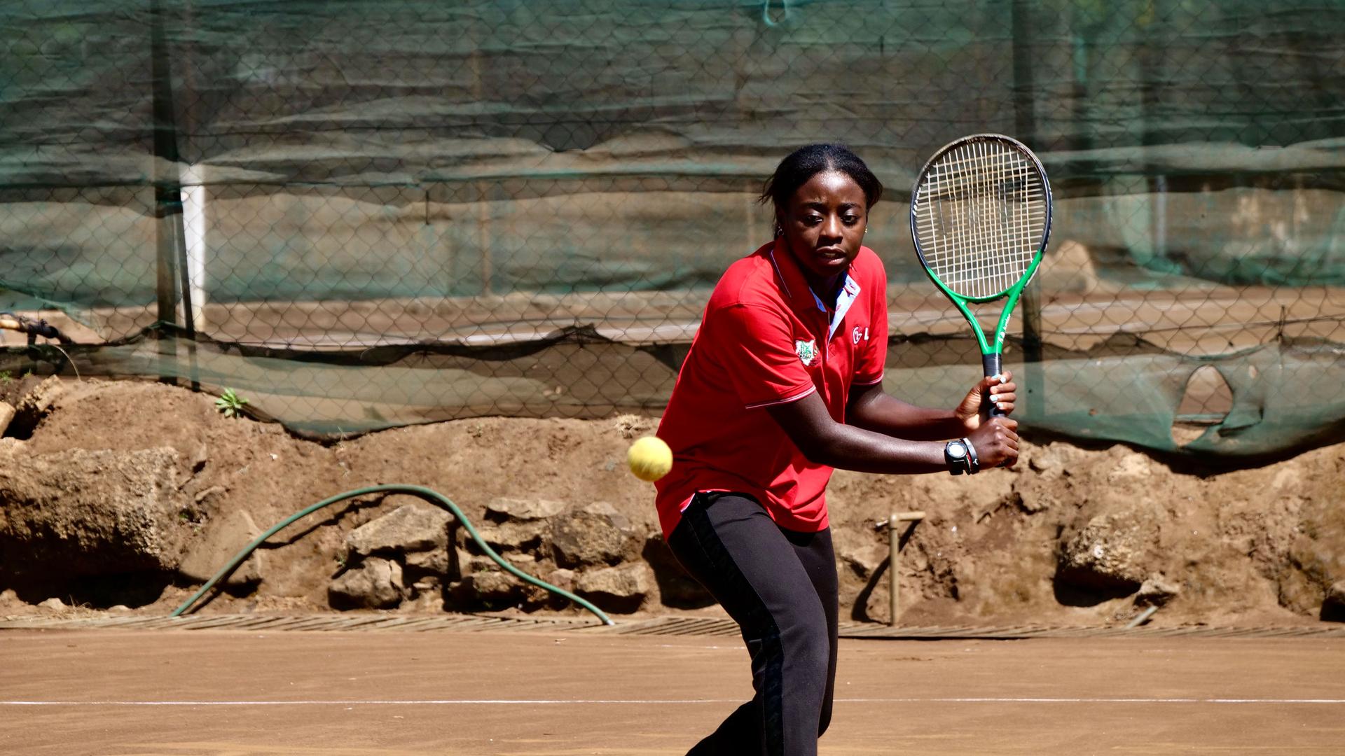 Angella Okutoyi, 18, seen wearing a red shirt and swinging a ball with her racket, is Kenya's fastest-rising tennis star. 