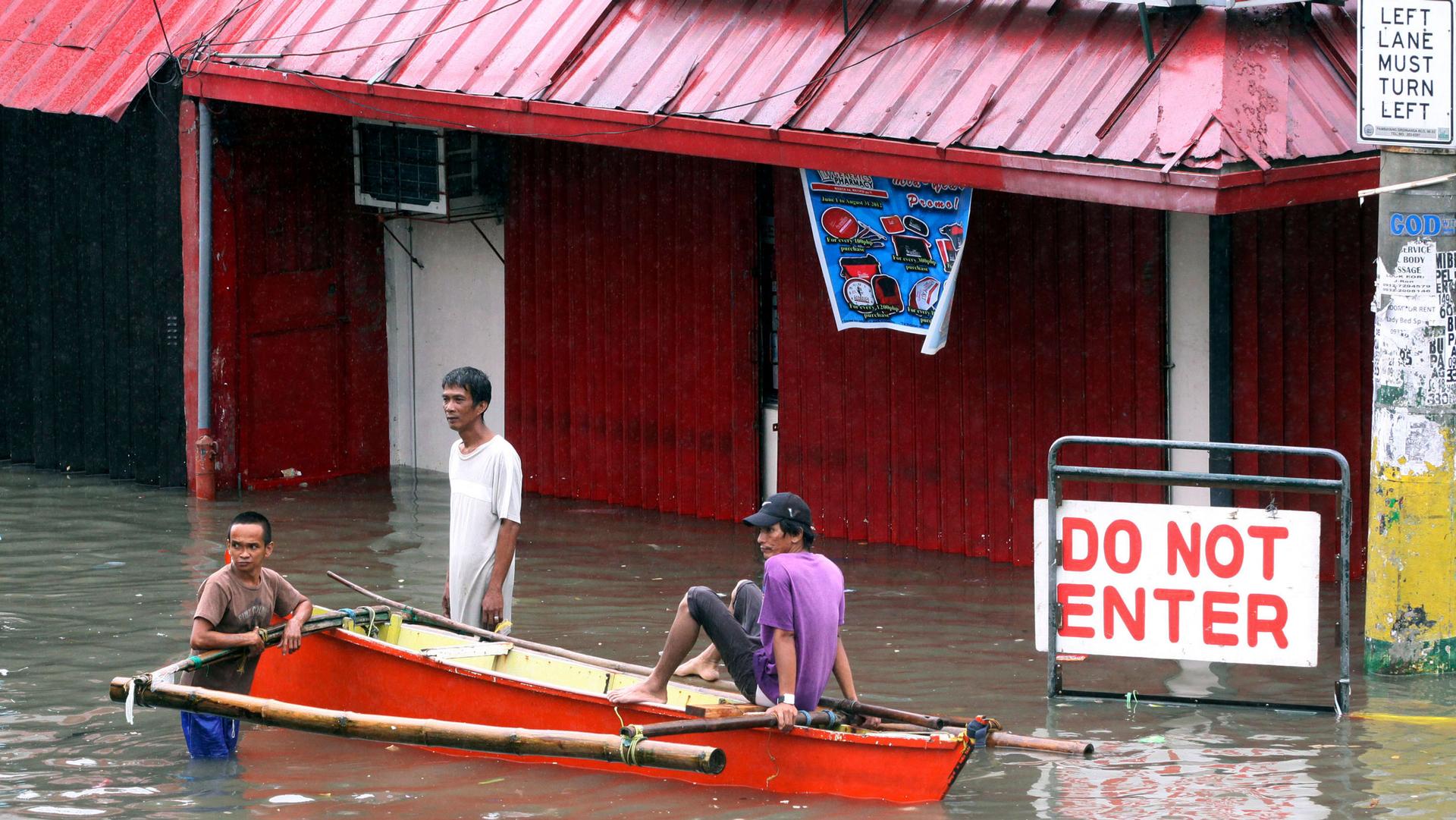 Three men huddle around their outrigger while waiting for passengers as flood waters continue to rise due to rain and high tide Thursday, Aug. 2, 2012, in Navotas City, north of Manila, Philippines. 