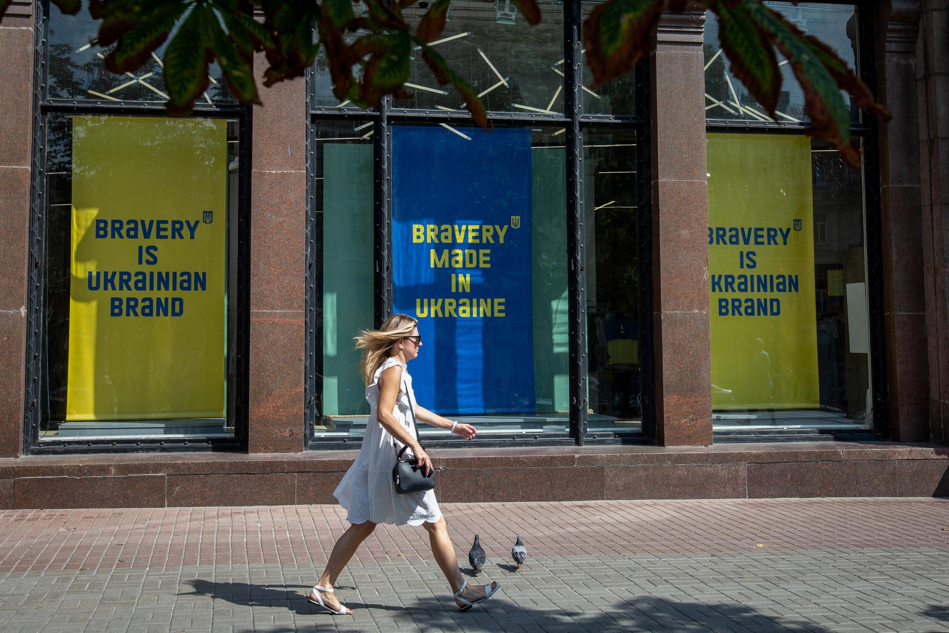 A woman strides down a street in front of Ukrainian yellow and blue banners with the branded slogans on them