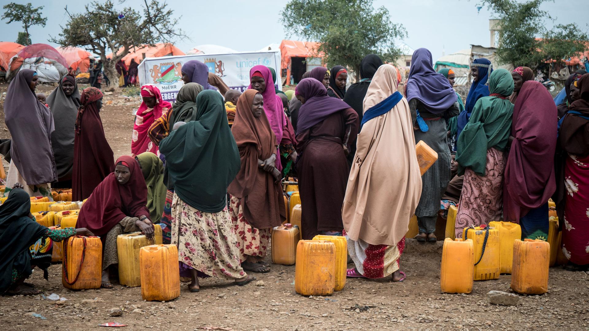 Displaced women collect water in yellow plastic cans in Baidoa, Somalia. 