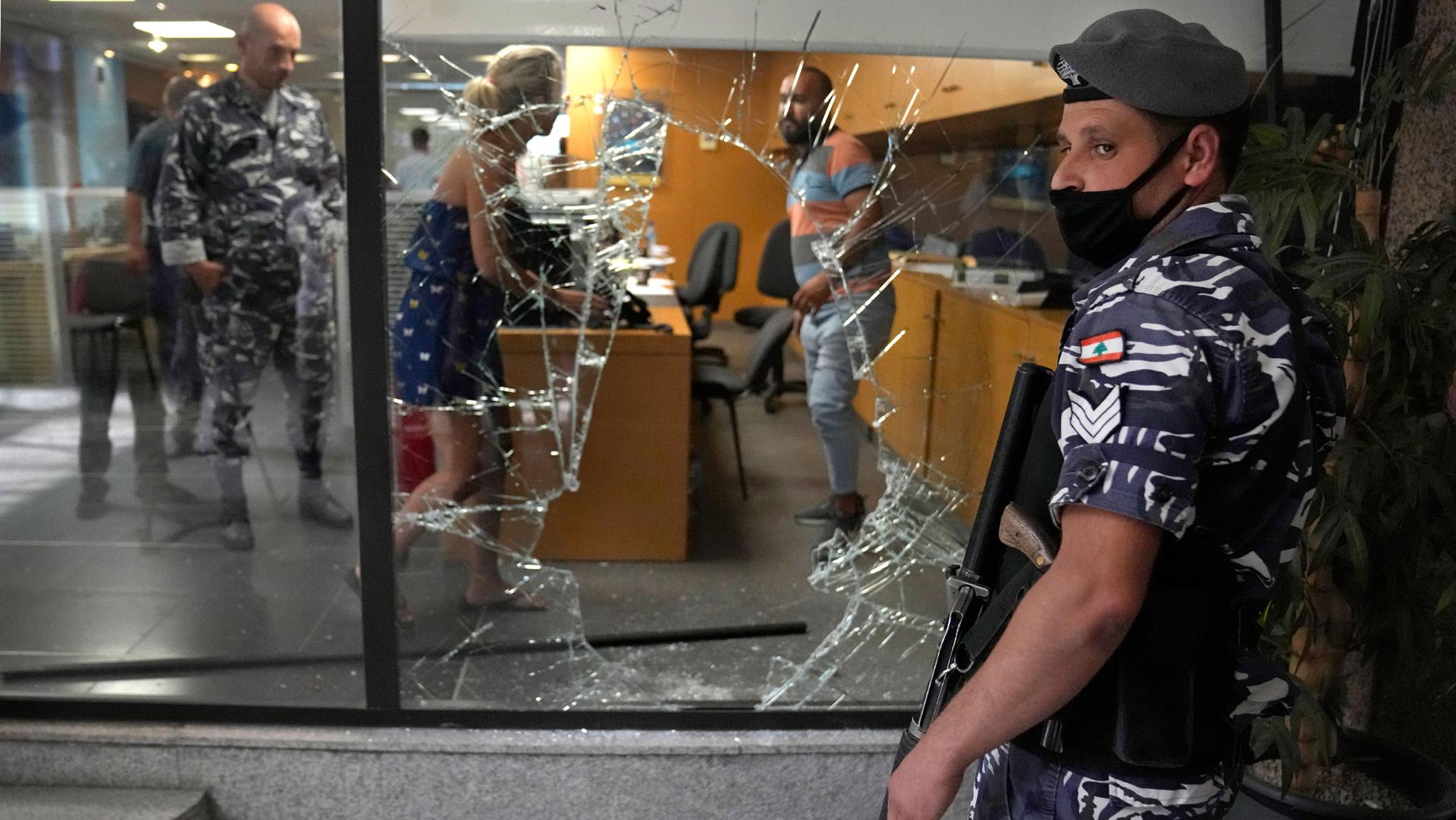 A Lebanese policeman stands guard next to a bank window that was broken by depositors to exit the bank after attacking it trying to get their money, in Beirut, Lebanon