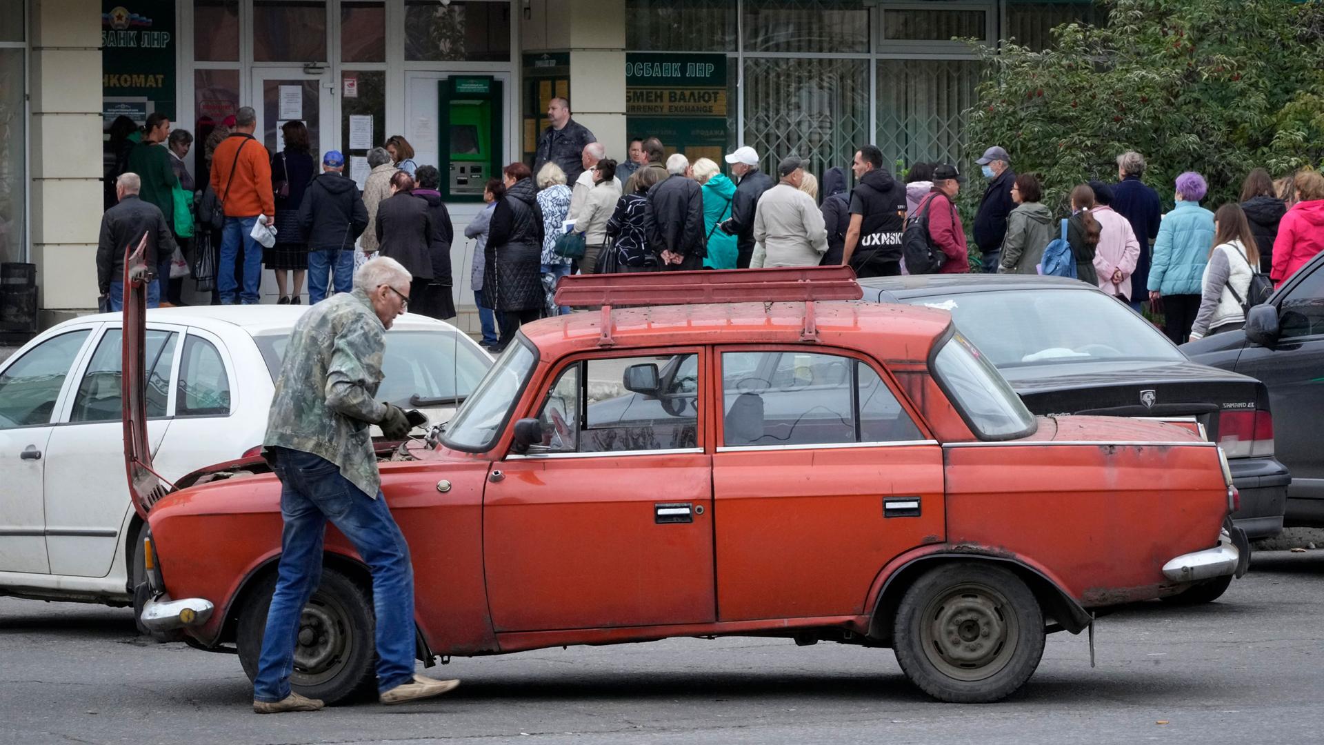 A man repairs his car as people line up to an office of Luhansk People's Republic state bank, a day after voting in four Moscow-held regions of Ukraine on referendums to become part of Russia, in Luhansk. 