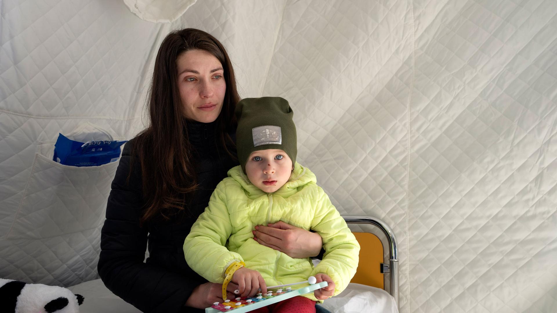 Anastasia, 3, is held by her mother, as she receives treatment at a schoolhouse that has been converted into a field hospital, in Mostyska, western Ukraine, Thursday, March 24, 2022. 