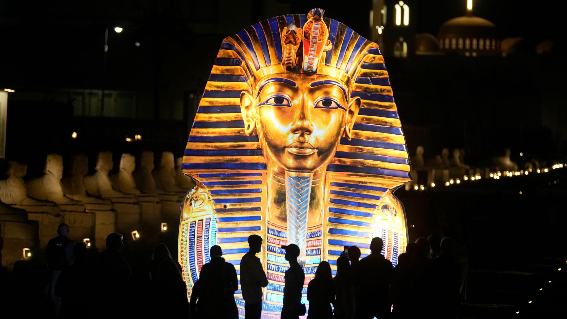 Tourists stand in front of a giant banner showing the golden mask of King Tutankhamun at Luxor temple in Luxor, Egypt, Nov. 4, 2022. 
