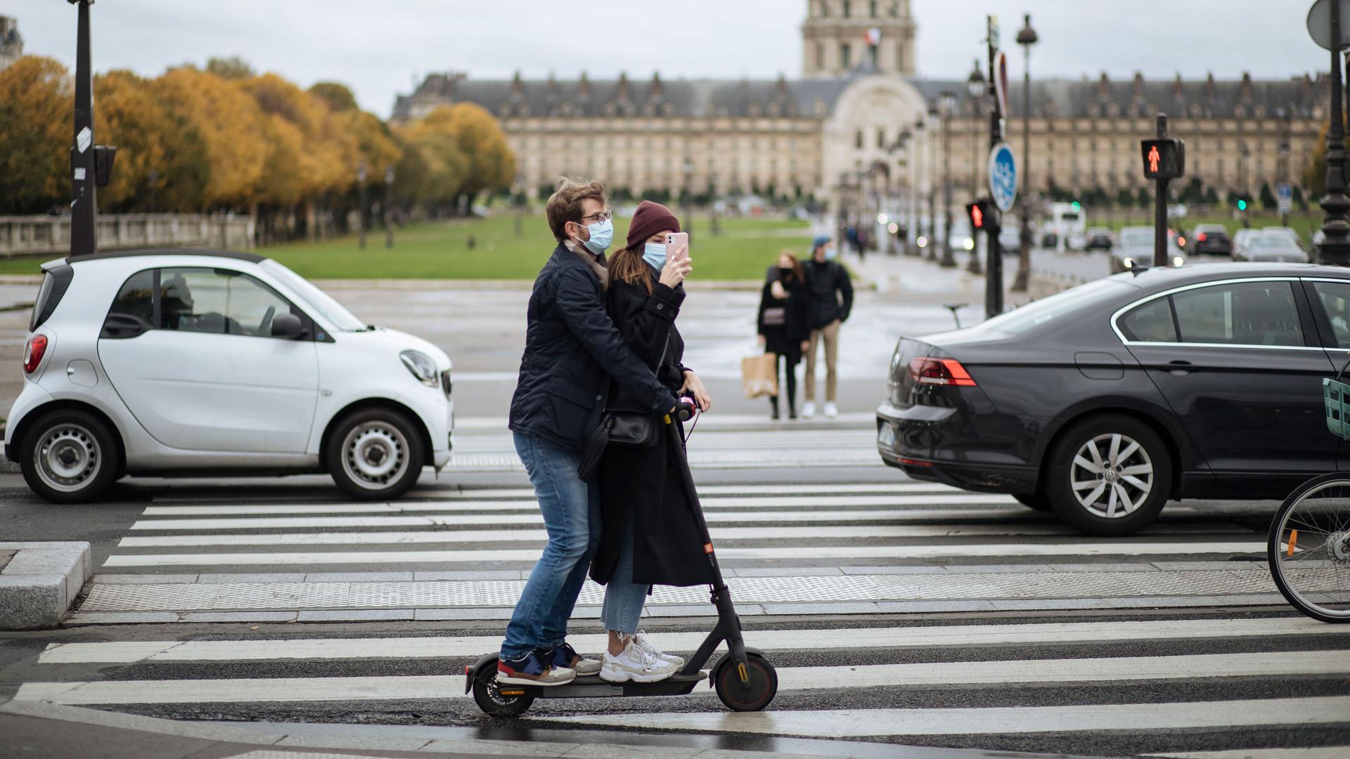 A masked couple ride an electric scooter by the Invalides memorial, in Paris, Sunday, Oct. 25, 2020. 