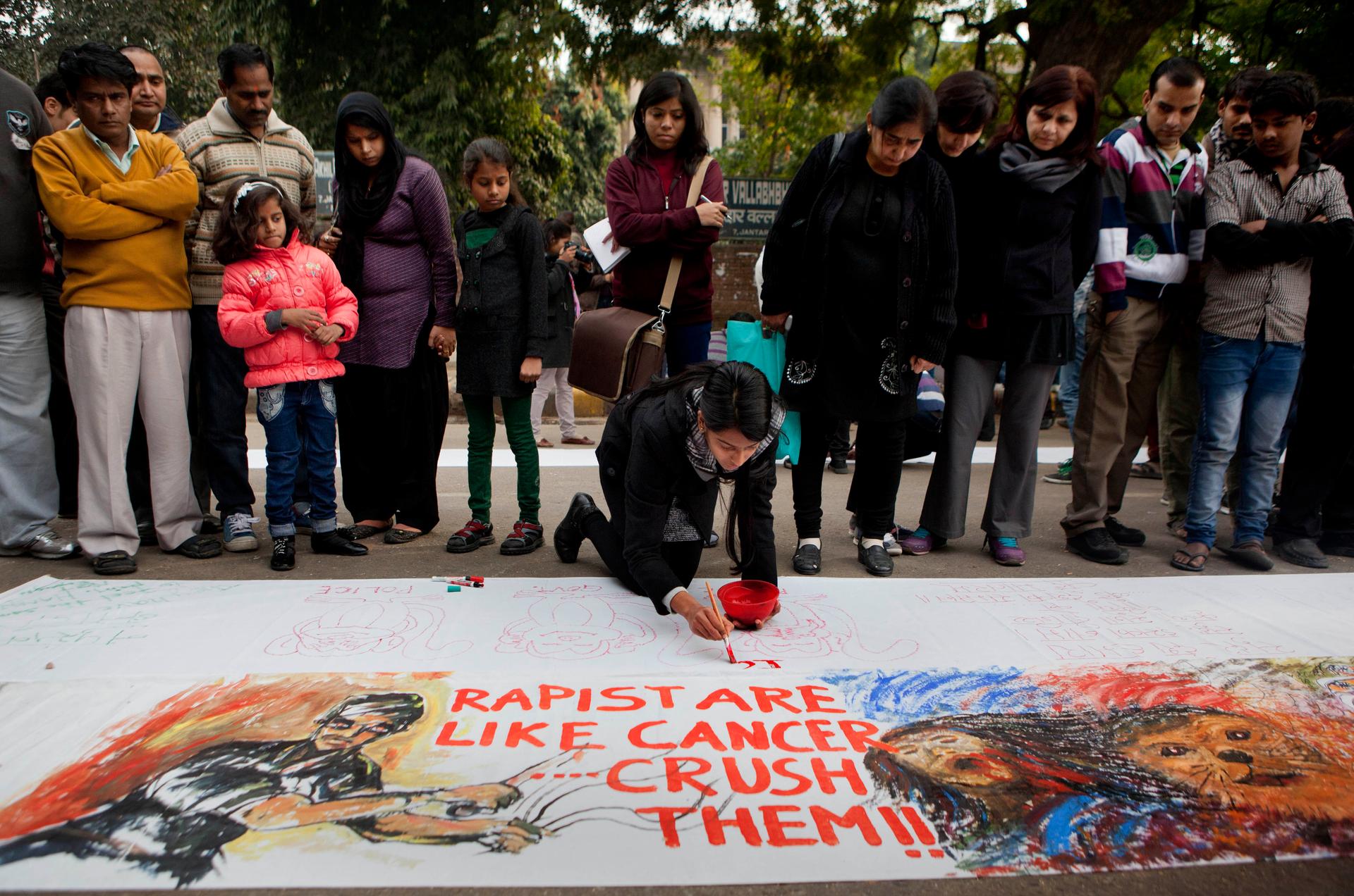 Indians watch a girl paint a message during a protest against the death of a young woman who was recently gang-raped, in New Delhi, India, Dec. 30, 2012.