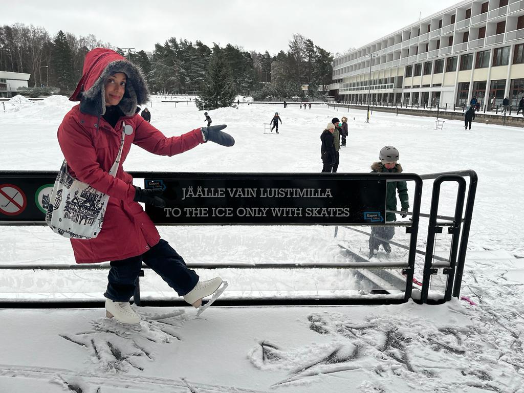 Kavita Pillay wears a red coat and stands near a sign that says "To the ice" in Finnish. 