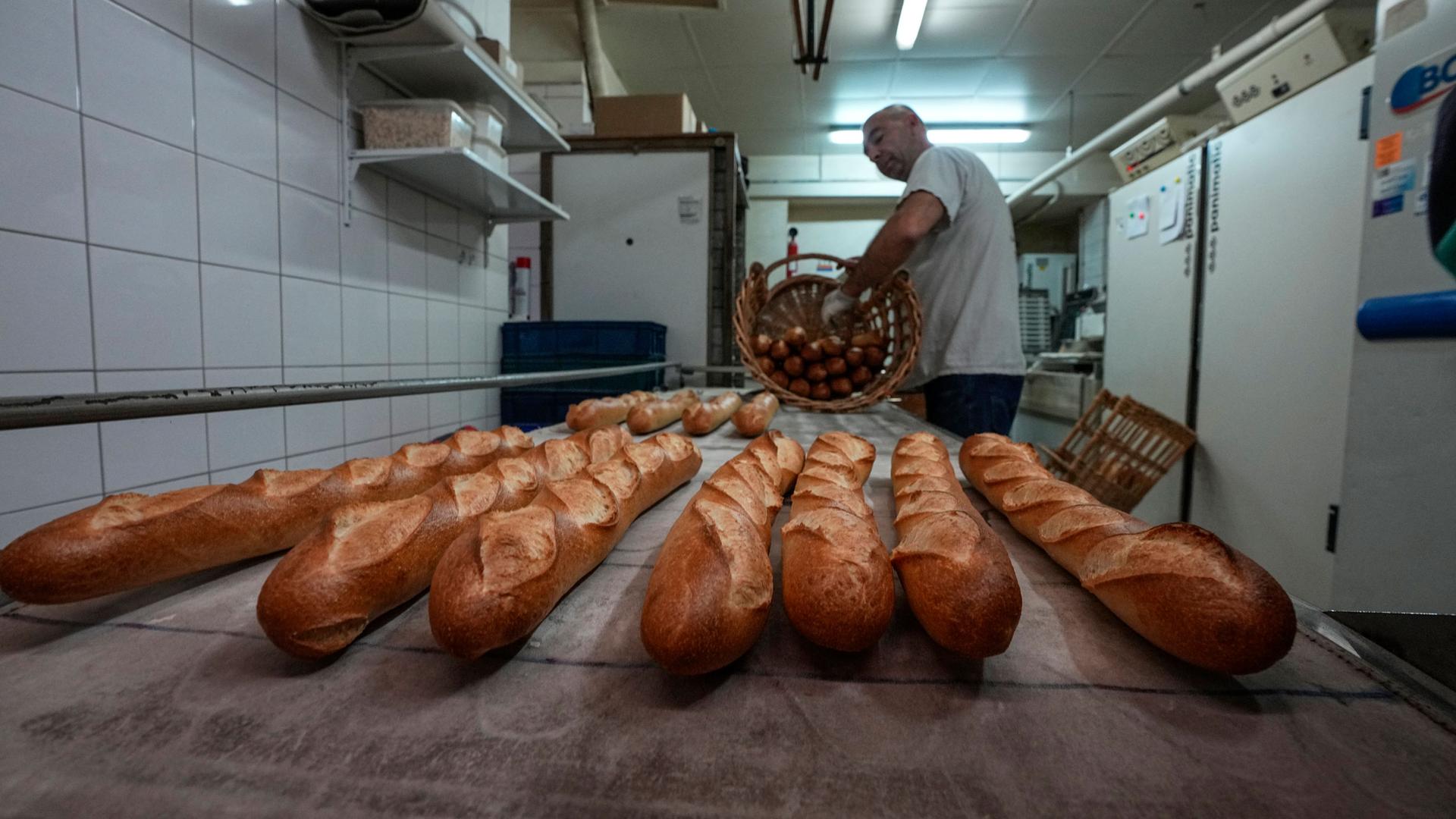 Baker David Buelens puts the baguettes into a basket at a bakery, in Versailles, west of Paris, Tuesday, Nov. 29, 2022. 