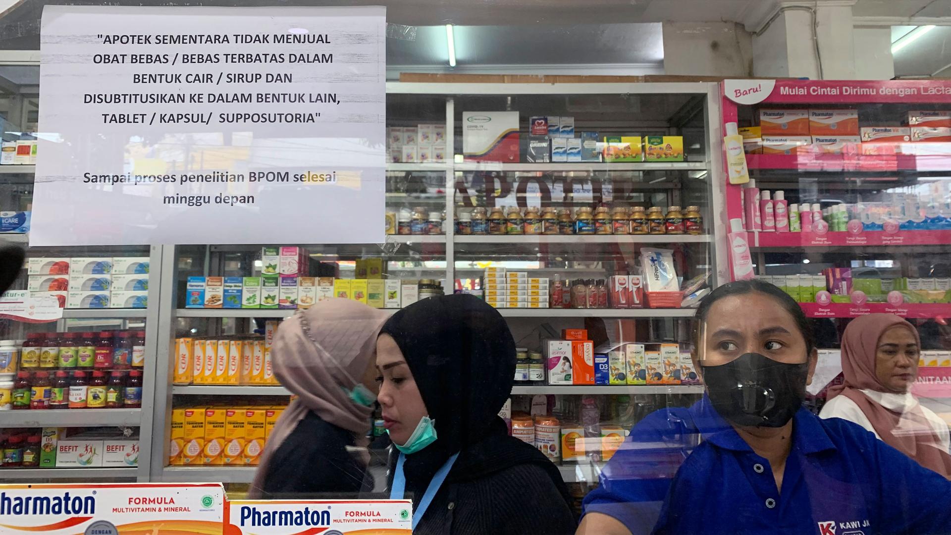 Employees wait for customers at a counter displaying a notification saying that the sale of medicinal syrup is temporarily halted at a pharmacy in Jakarta, Indonesia, Thursday, Oct. 20, 2022. 