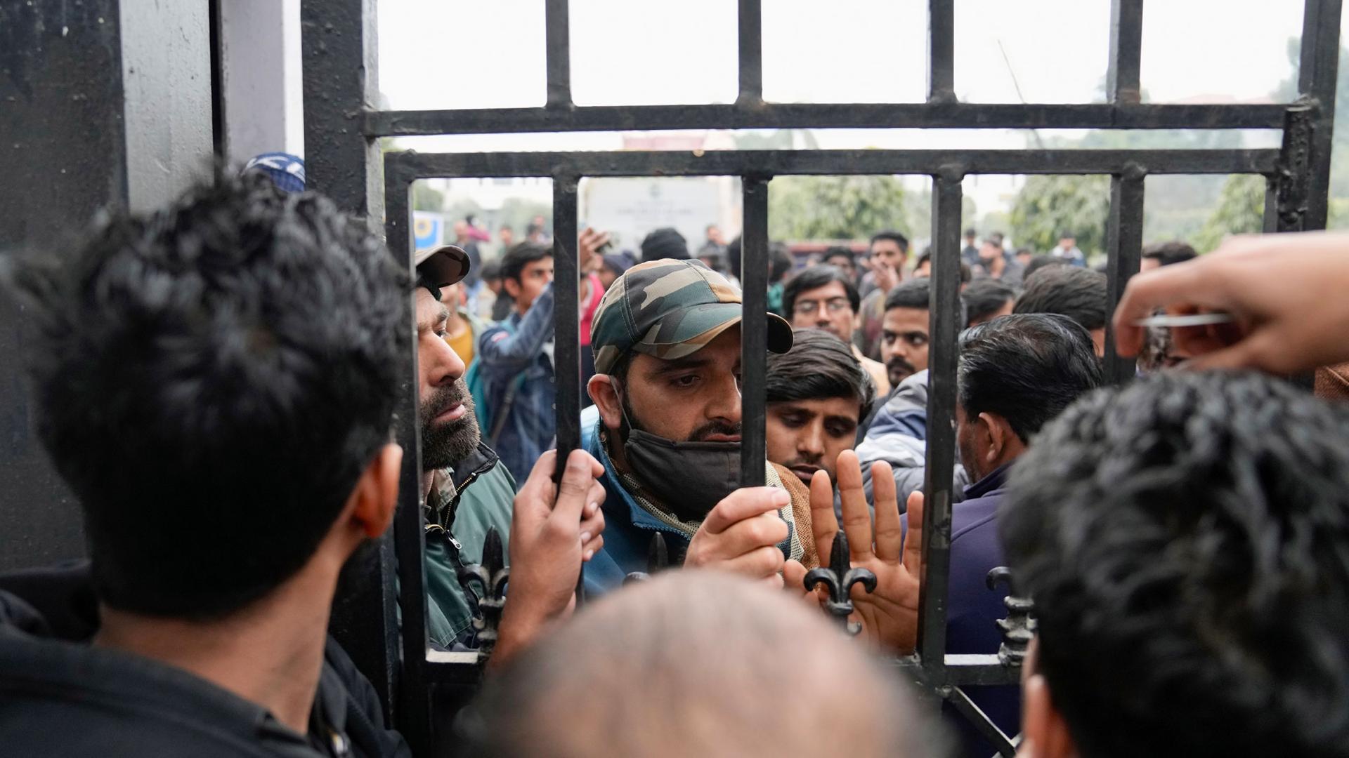 A security personnel speaks to people from inside the main gate of Jamia Millia Islamia university in New Delhi, India