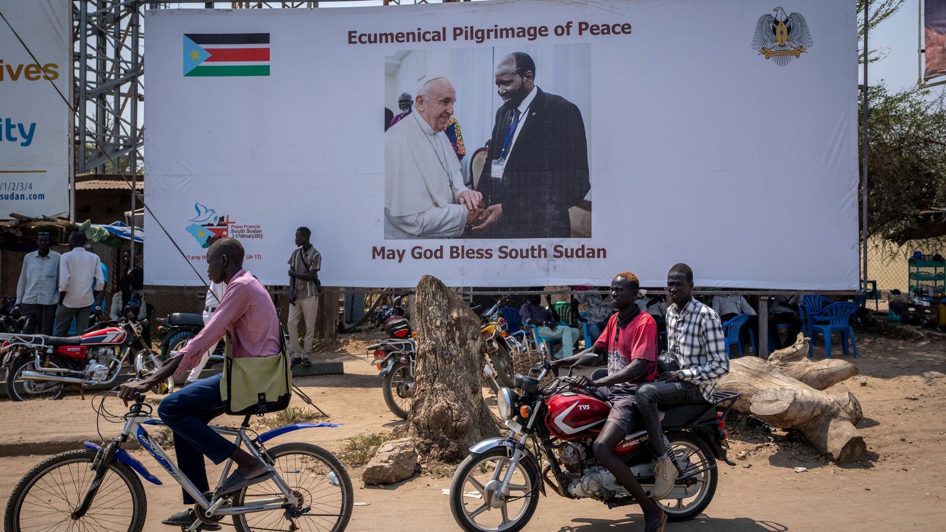 A motorcyclist passes a poster showing Pope Francis and South Sudan's President Salva Kiir, on a street in Juba, South Sudan Wednesday, Feb. 1, 2023. 