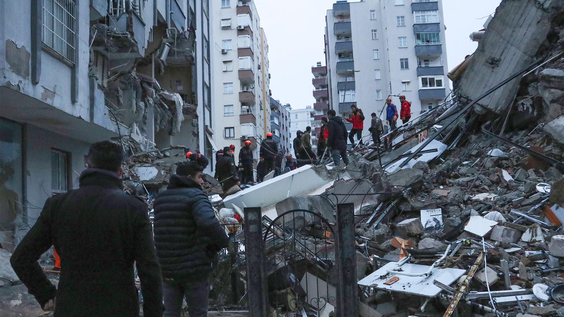 People and rescue teams try to reach trapped residents inside collapsed buildings in Adana, Turkey, Feb. 6, 2023.