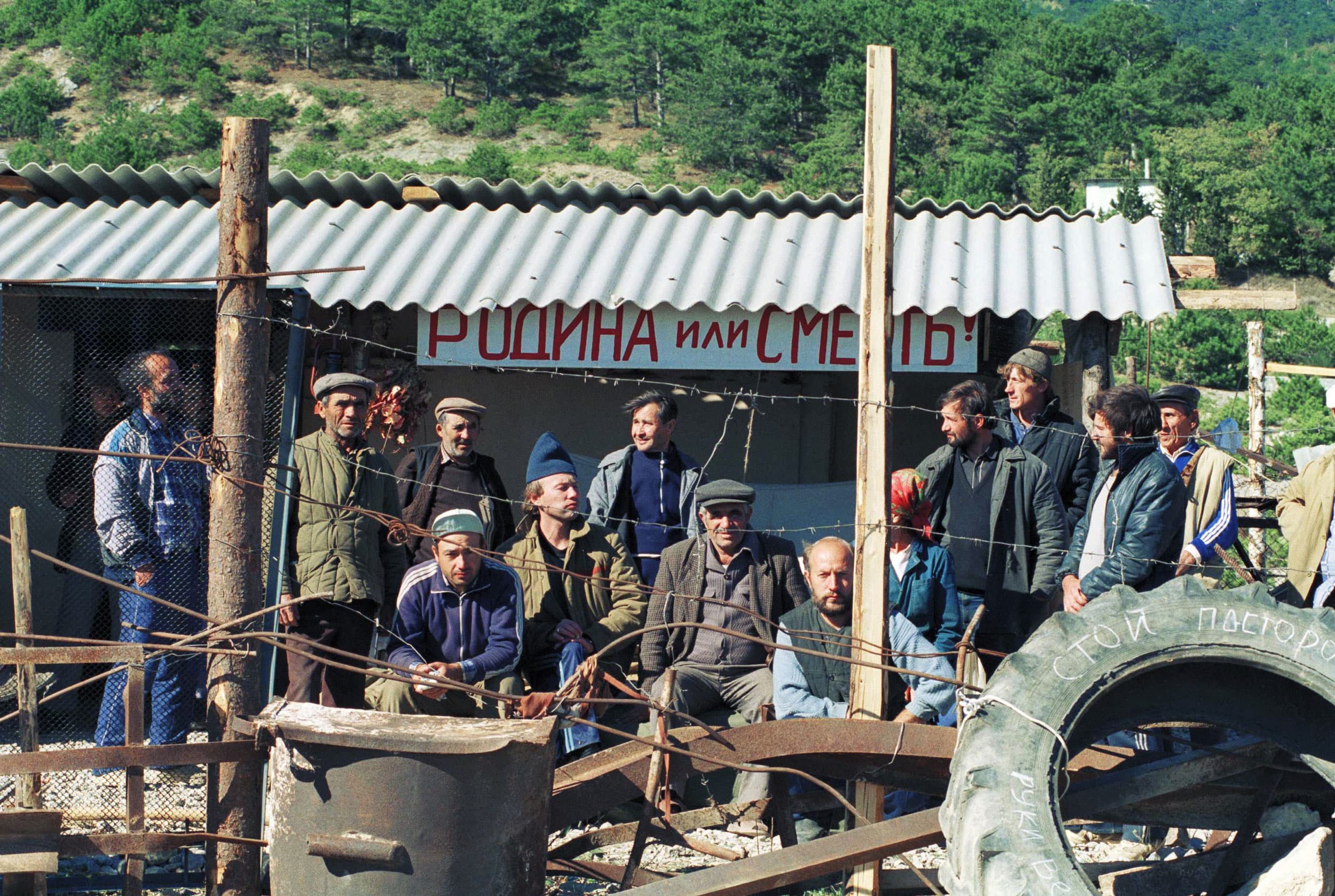 Some of 100,000 Crimean Tatars who returned to their native land stare from behind a barbed wire fence in Crimea on Sunday, Oct. 30, 1990. The slogan reads