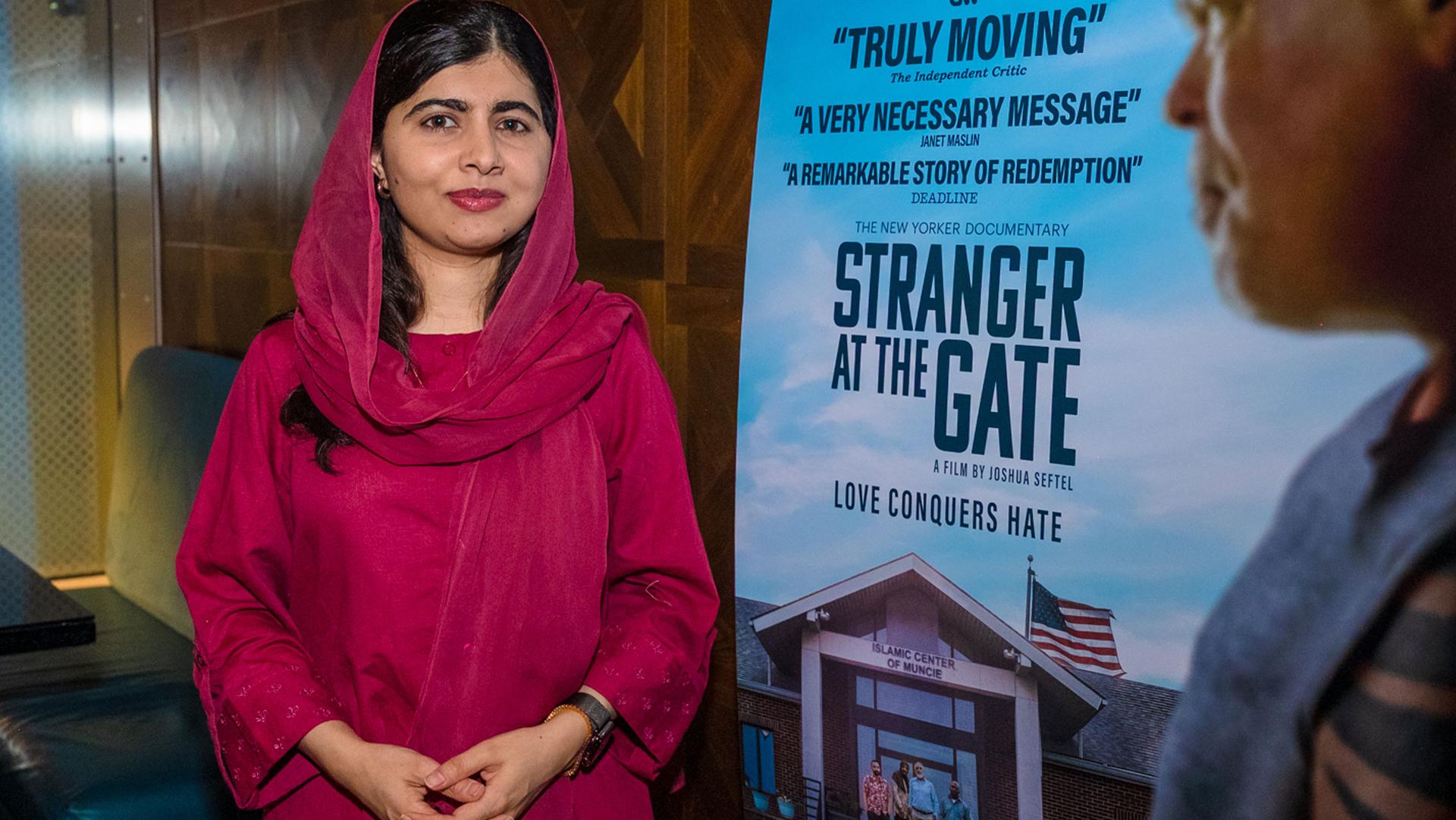 Malala Yousafzai pointing at a poster advertisement of her documentary, "Stranger at the Gate."